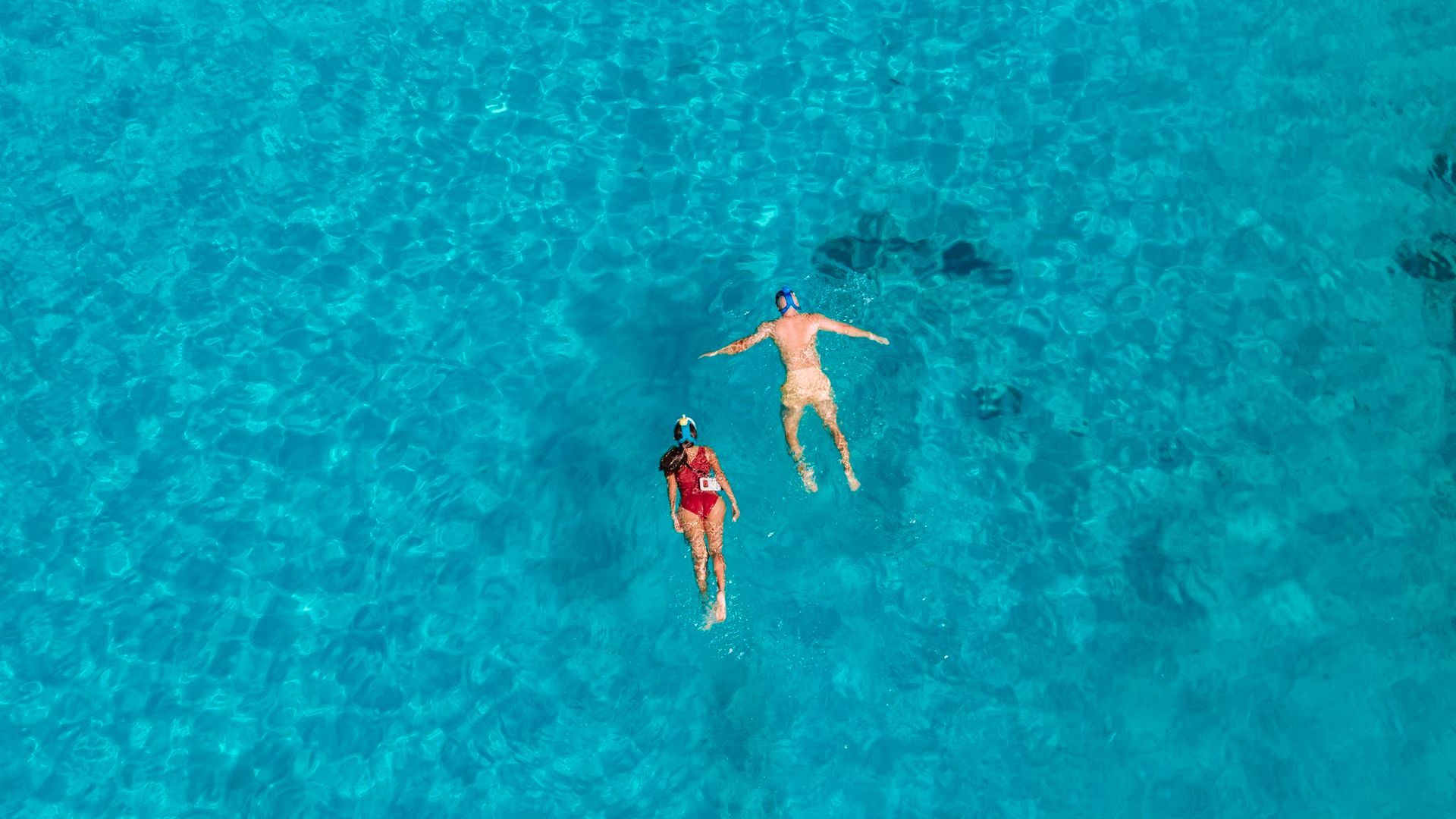 Deux personnes font de la plongée en apnée dans une eau bleue et limpide.