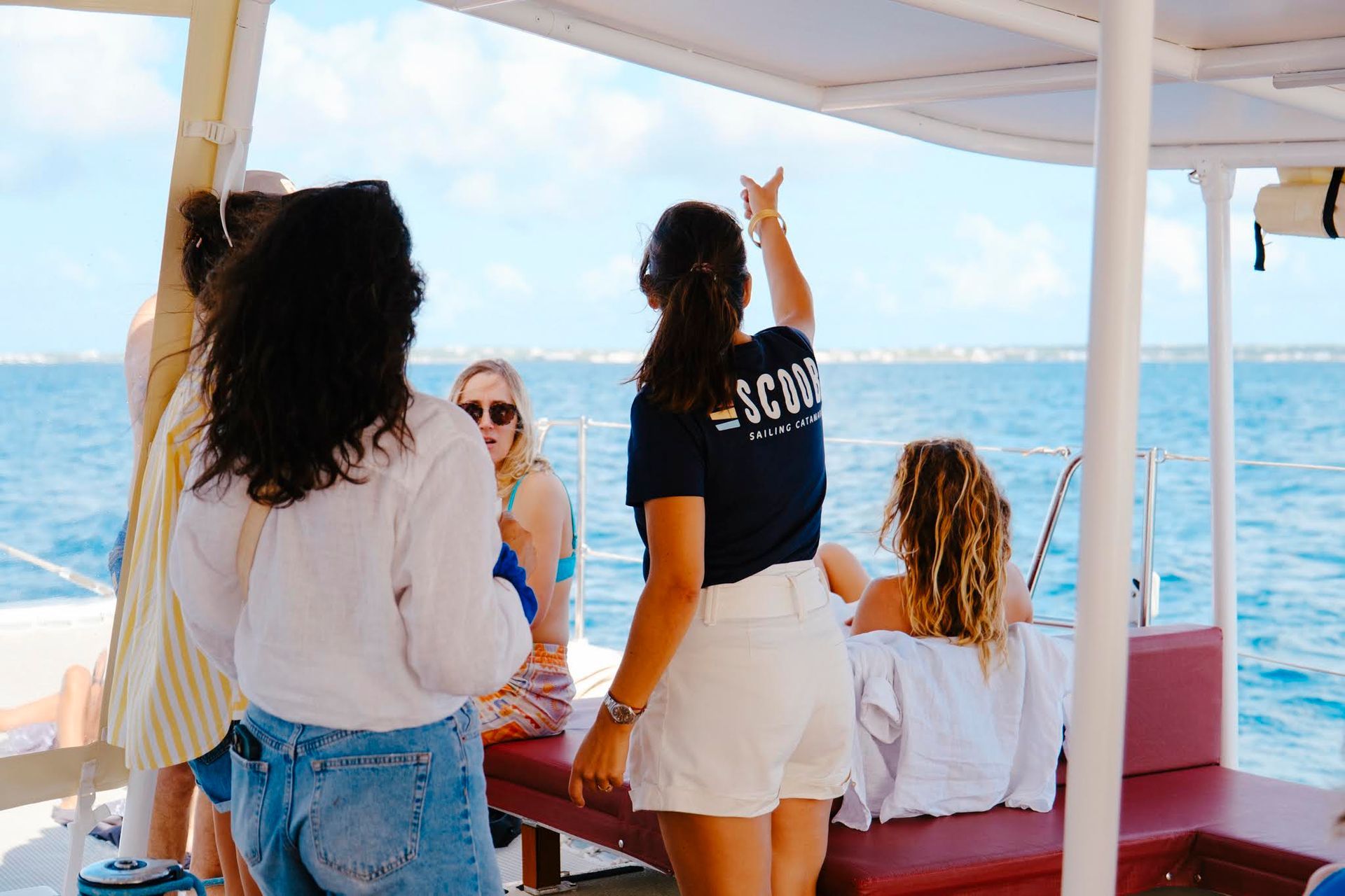 Un groupe de personnes sur un bateau, sur l'eau ; l'une d'elles pointe du doigt au loin.