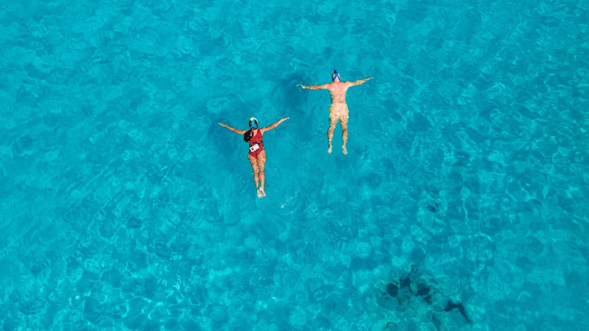 Deux personnes font de la plongée en apnée dans une eau d'un bleu éclatant, les bras tendus.