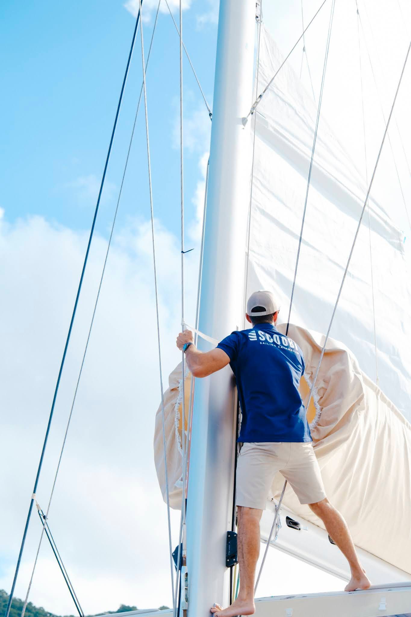 Man on sailboat adjusts rigging against a blue sky.