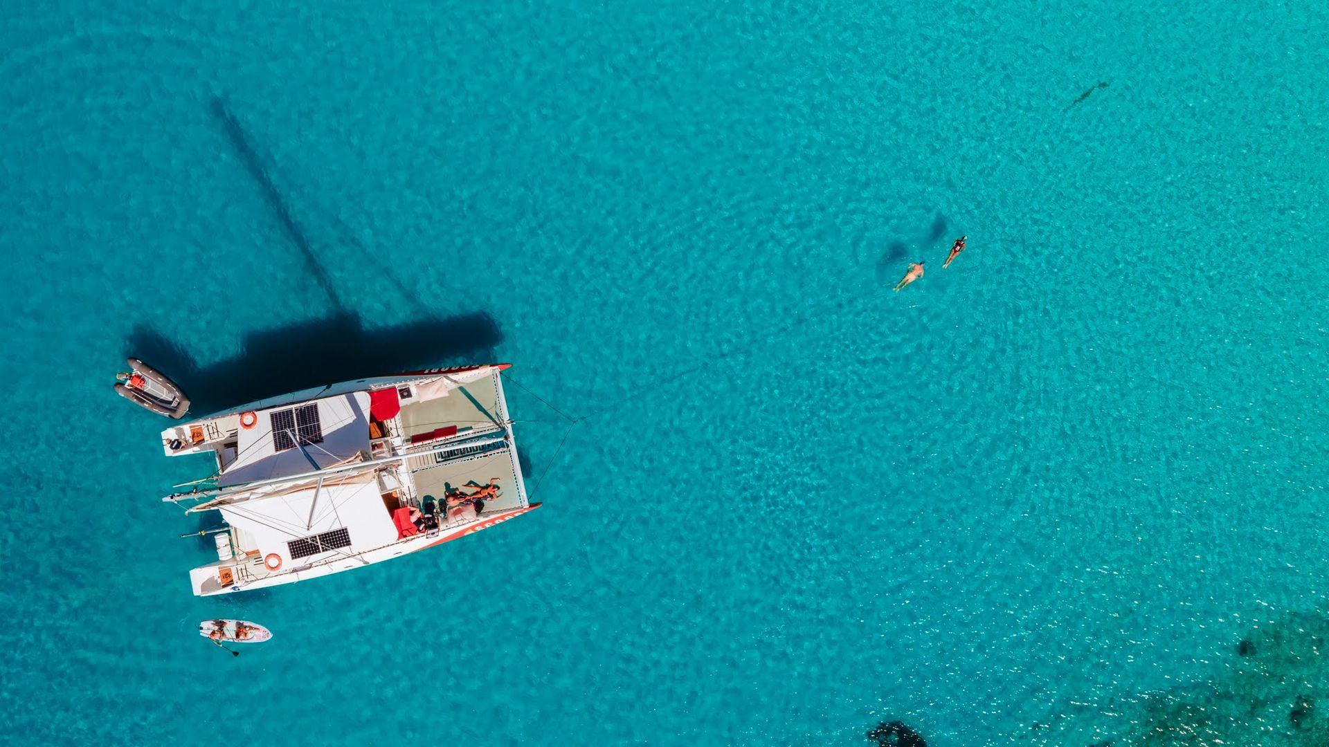 Catamaran in turquoise water with people swimming.