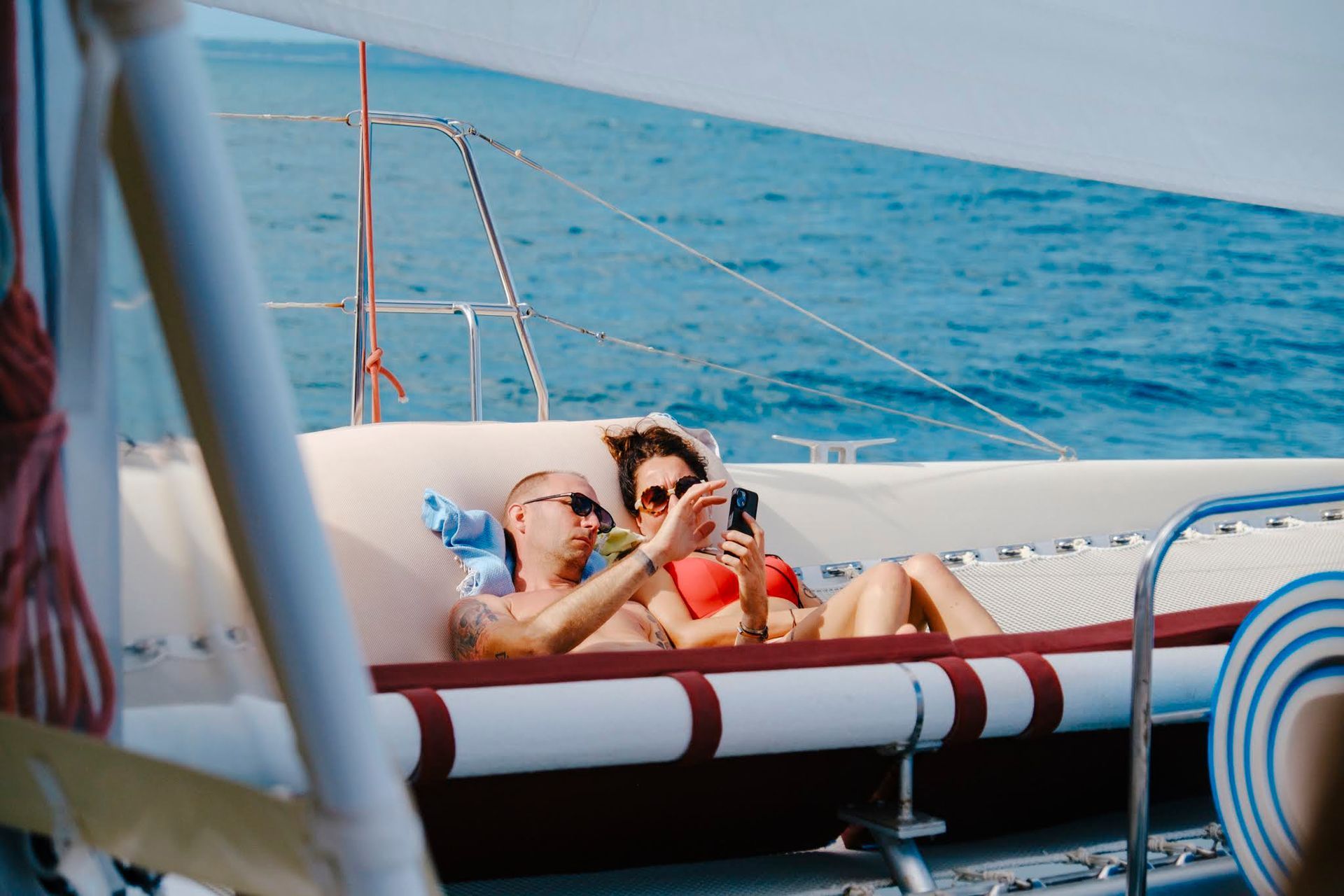 Couple on a yacht taking a selfie. They are in swimwear, relaxing on a cushioned deck with ocean in the background.