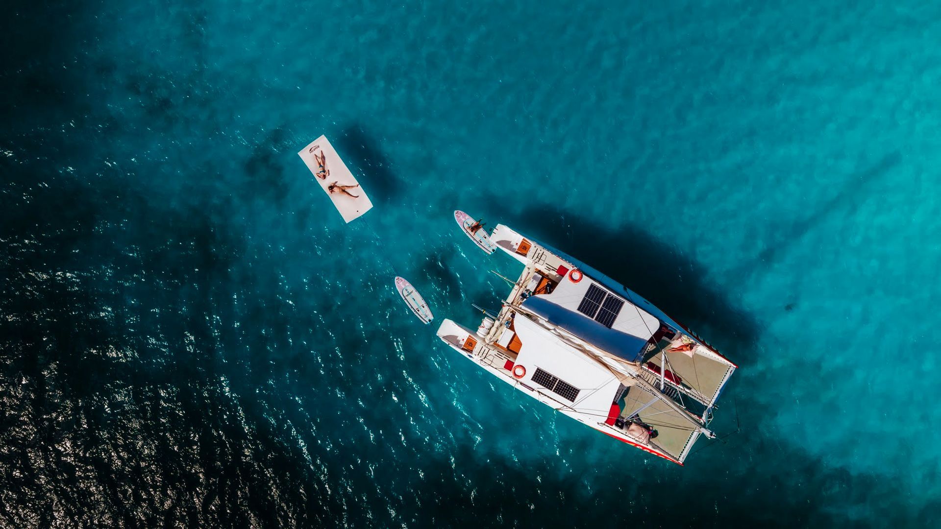 Catamaran and small raft on turquoise water, overhead view.