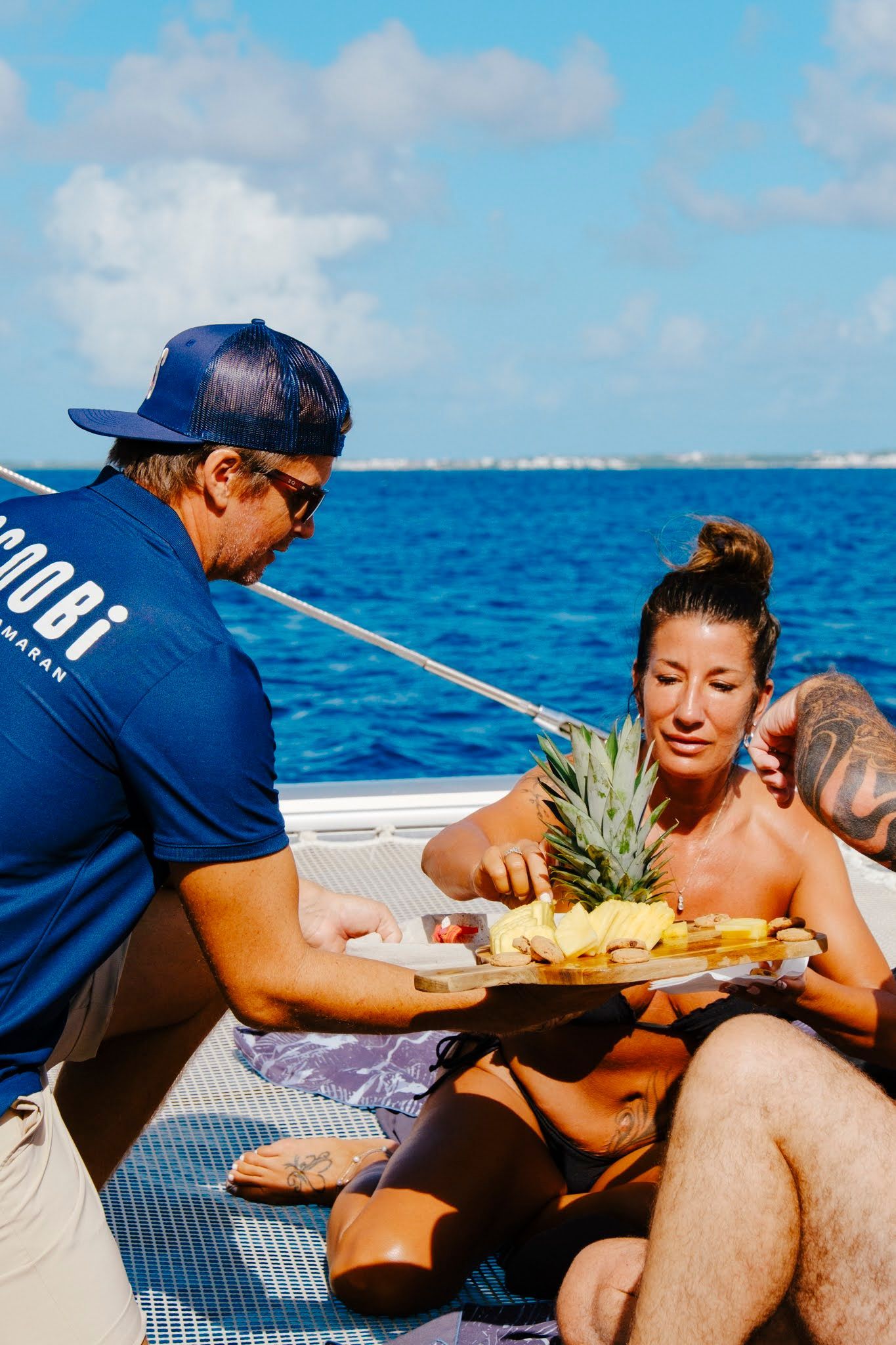 Man serving a plate of food to a woman on a boat. Ocean in background.