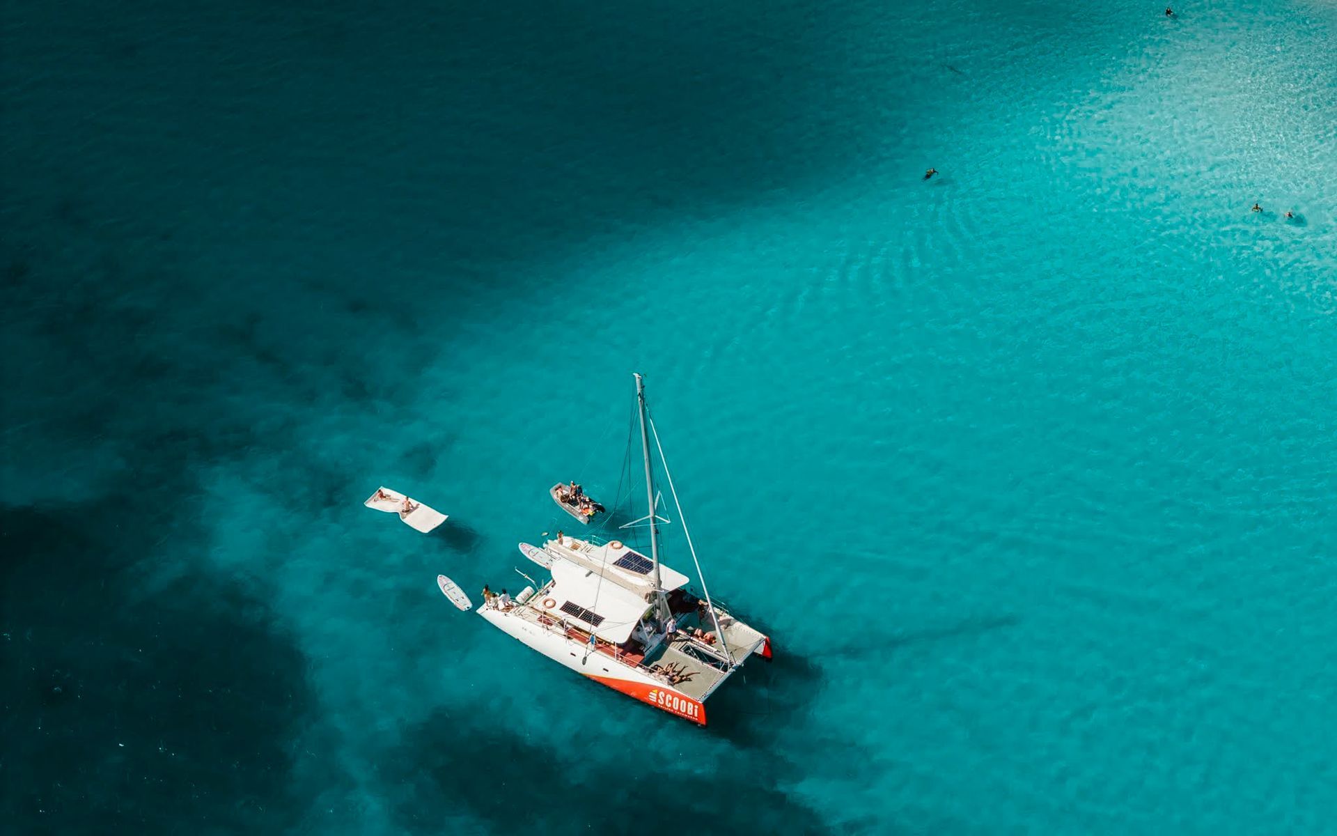 Catamaran sails on turquoise water near a sandy seabed.