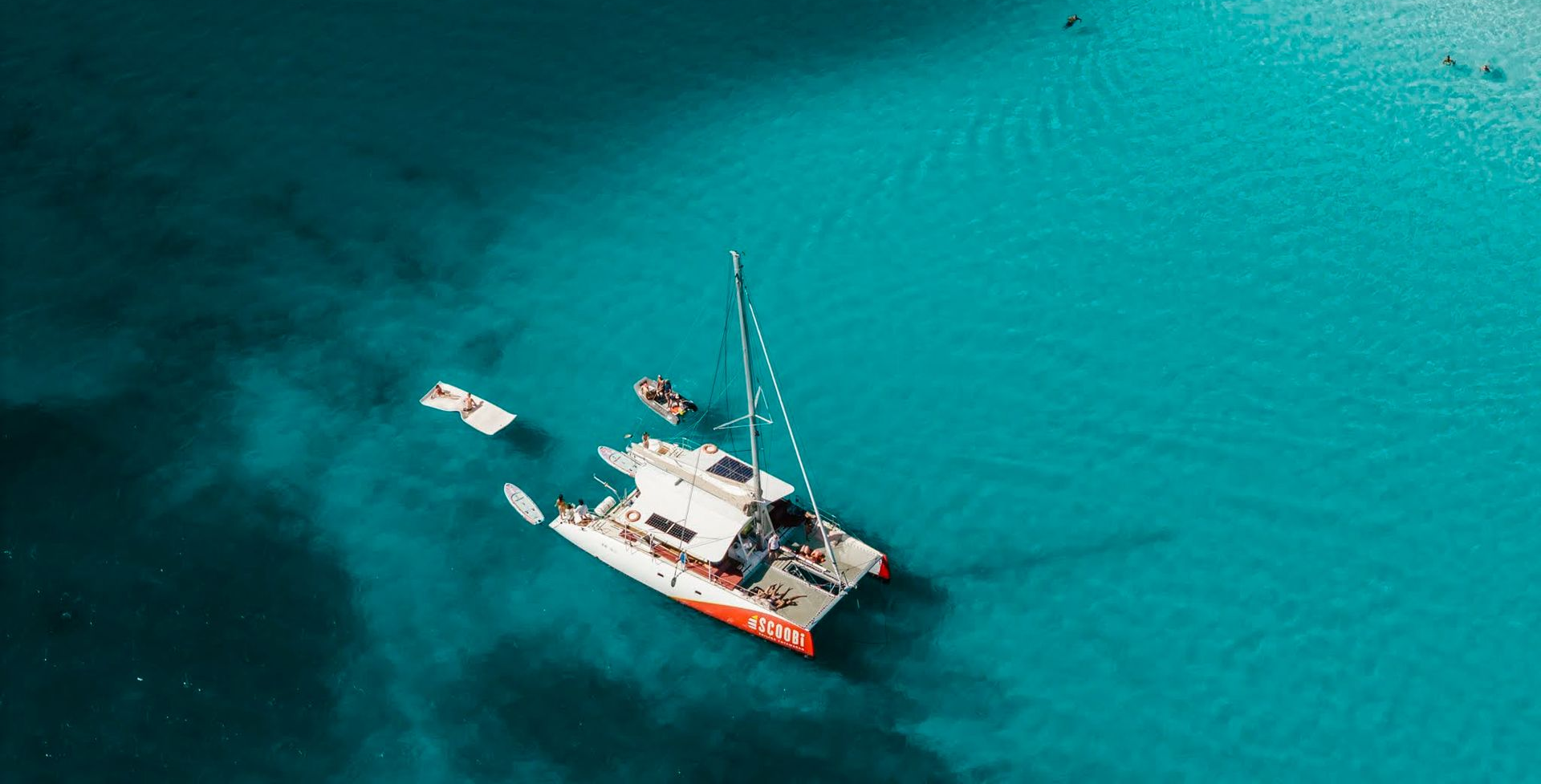 Catamaran and small boat in clear turquoise water.