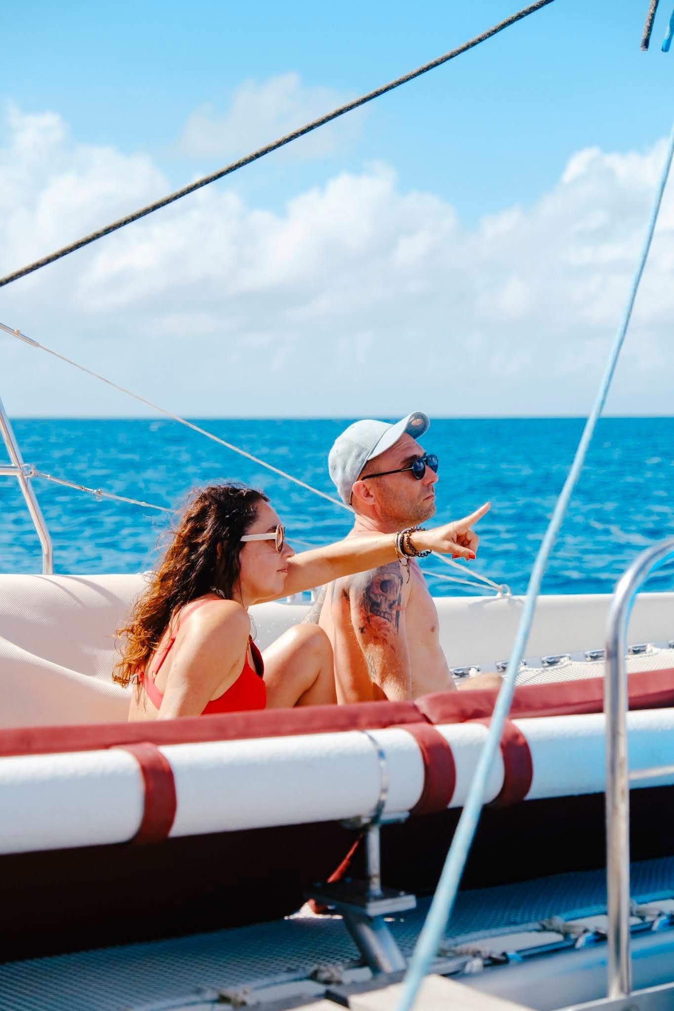 Couple on a sailboat, woman points at the blue ocean, sunny day.