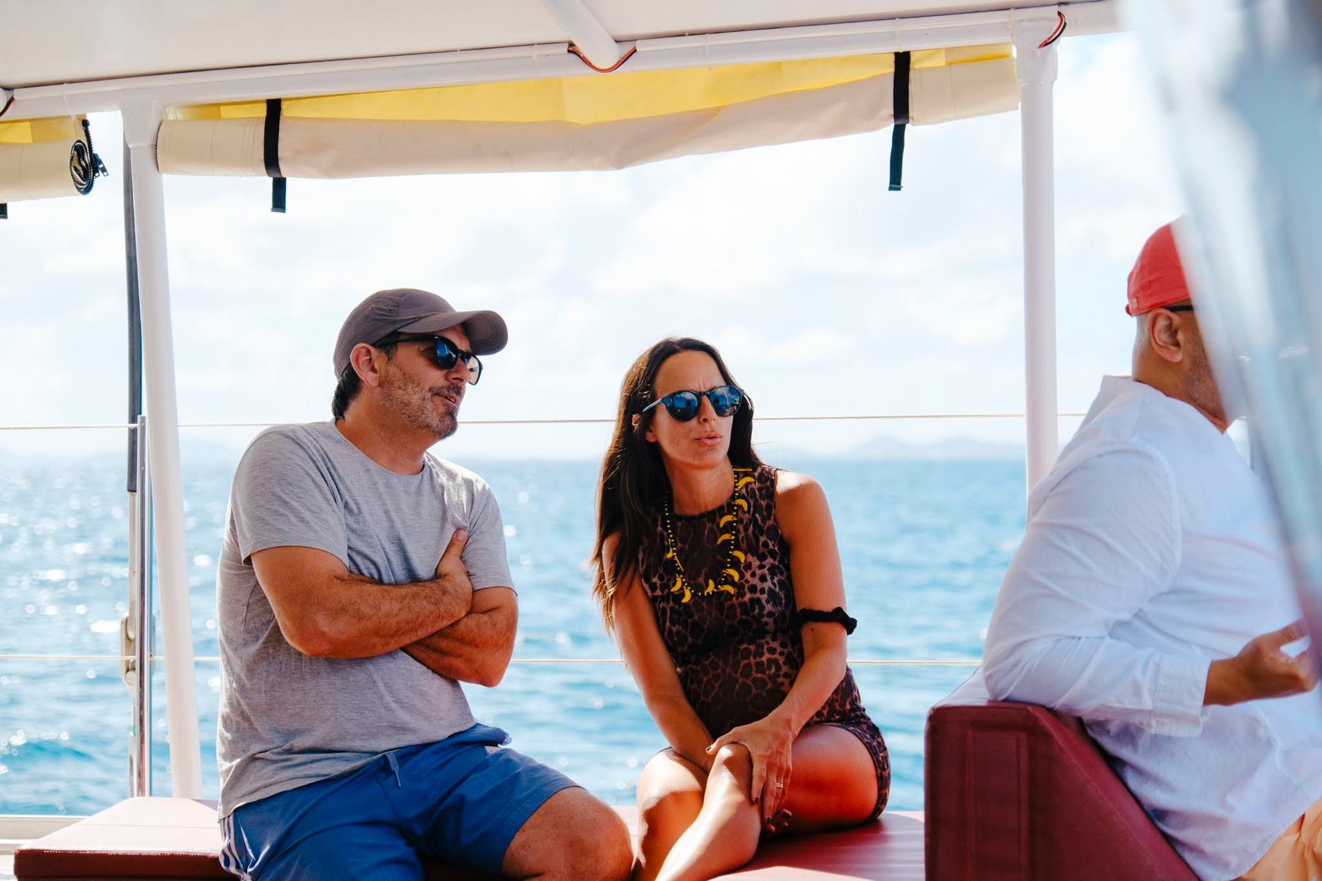 Trois personnes sur un bateau, la femme en robe à imprimé léopard portant des lunettes de soleil, vue sur l'océan.