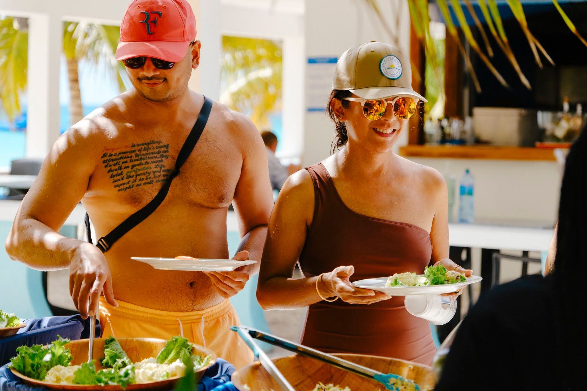 Man and woman at outdoor buffet, holding plates of food. 