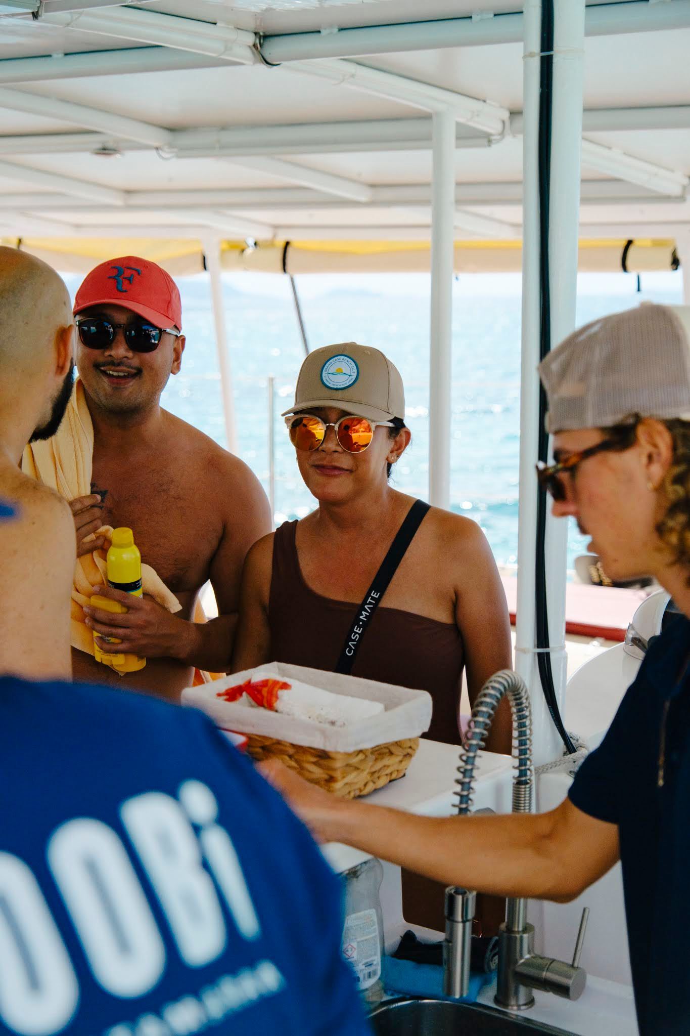 People on a boat near the ocean. One person holds a basket, others wear sunglasses and hats.
