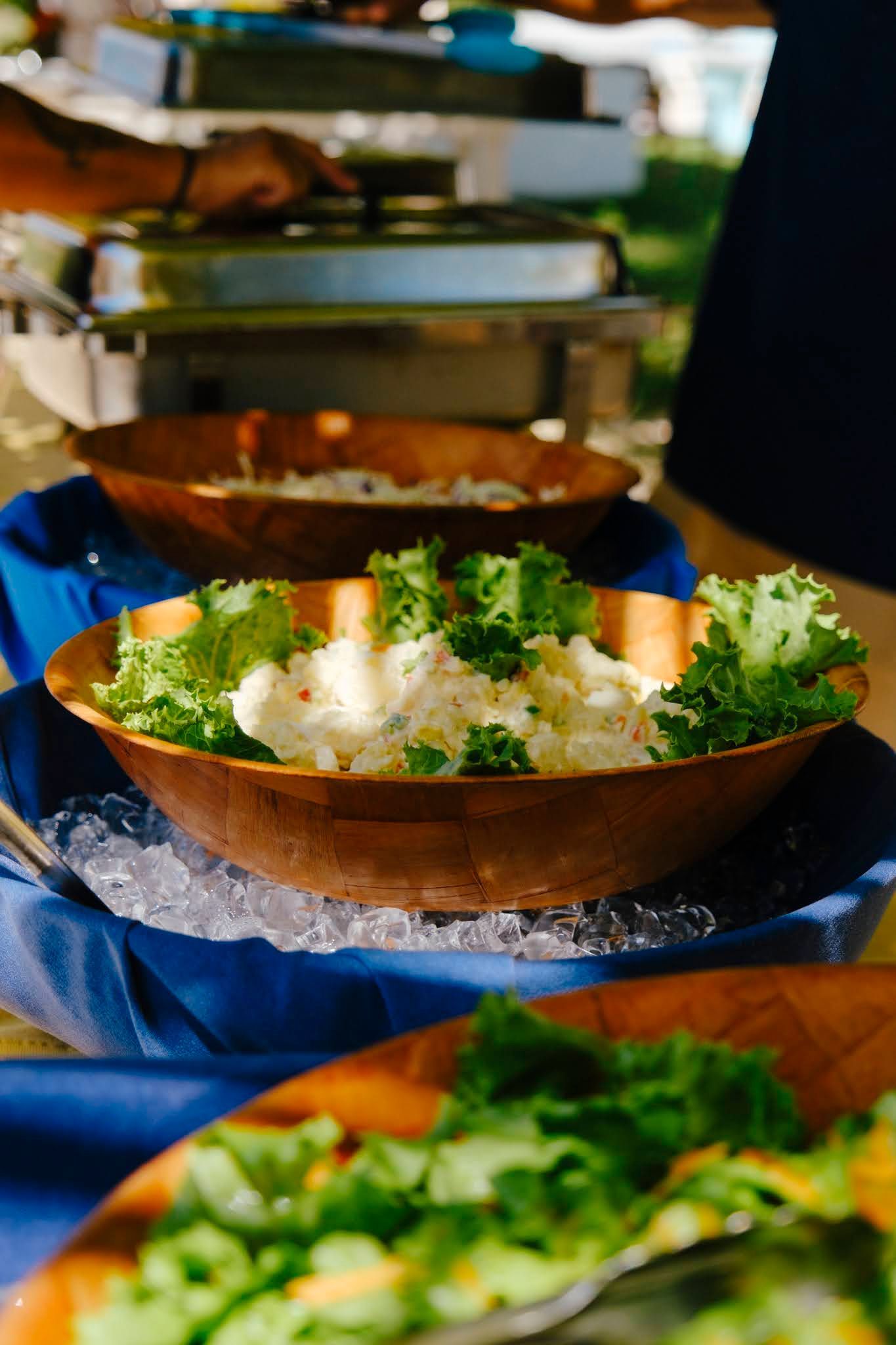 Buffet table with wooden bowls holding salad on ice.