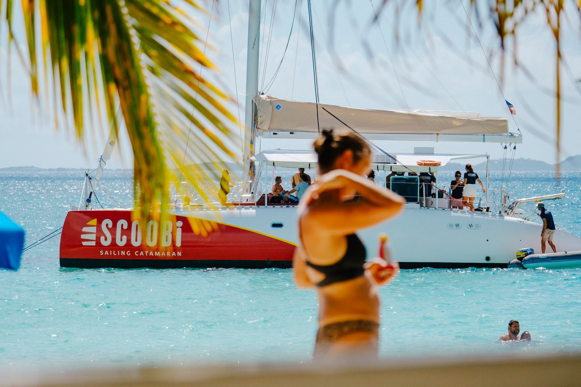 Woman applying sunscreen on beach with a catamaran that has 