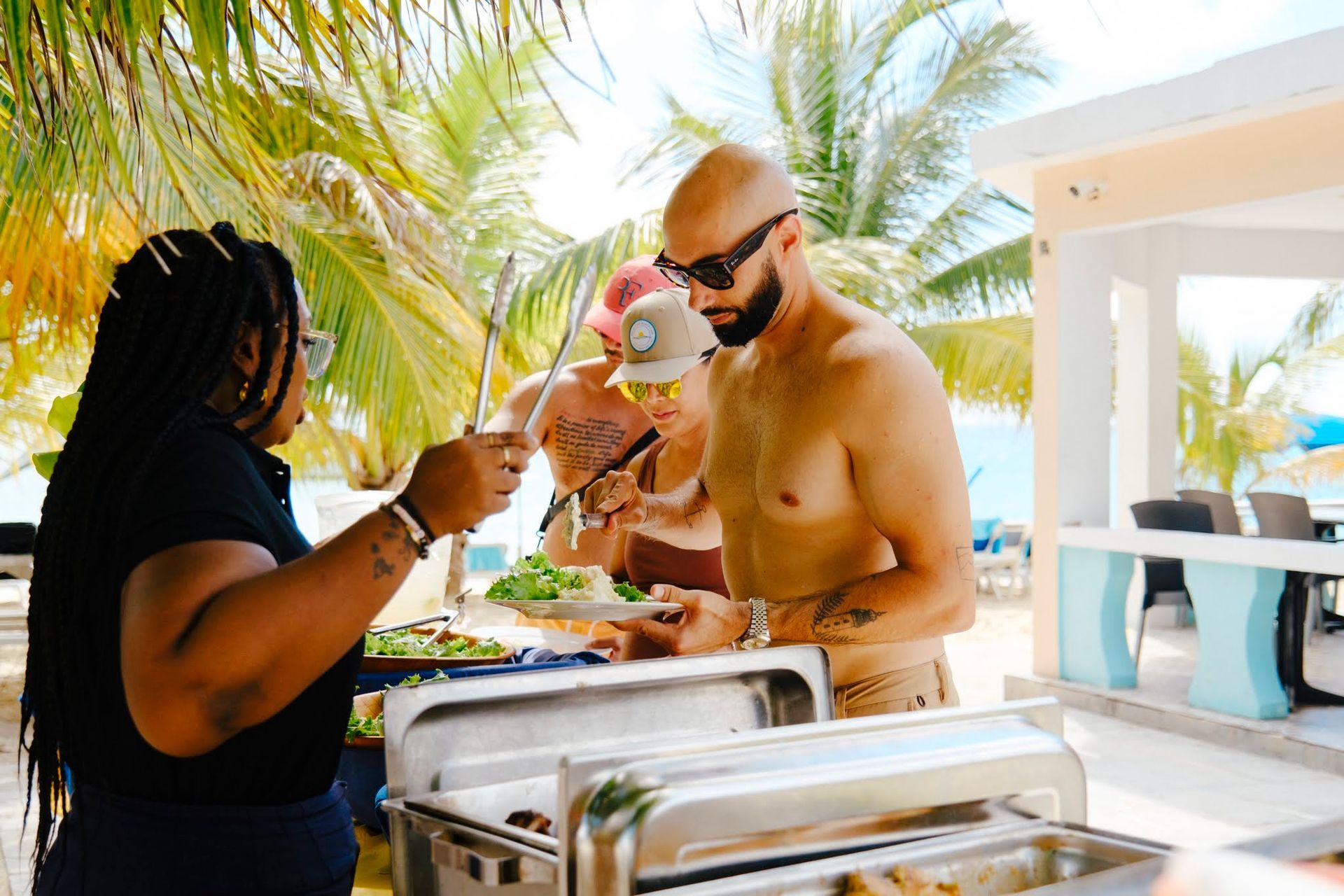 Des gens au buffet sur la plage, une personne sert, les autres se servent.