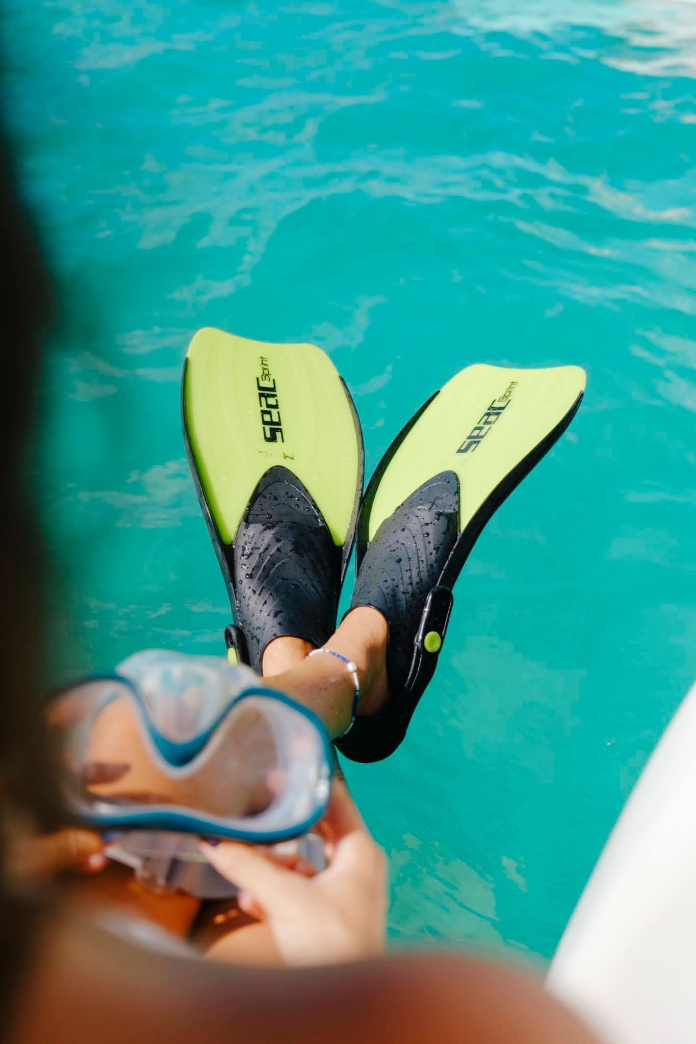 Person in turquoise water with lime green and black fins, holding a snorkel mask.