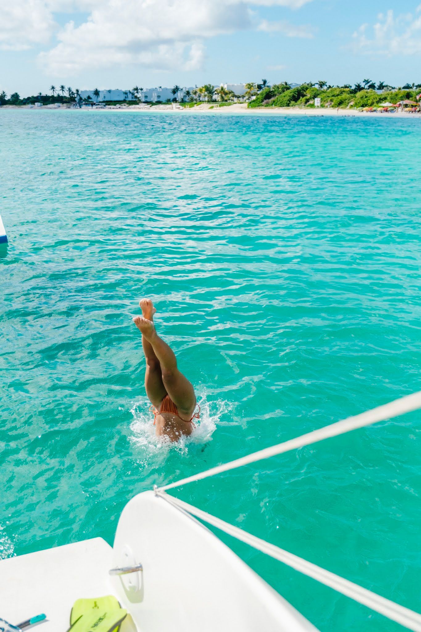 Person diving from a white boat into clear turquoise water. Sunny day with a coastal backdrop.