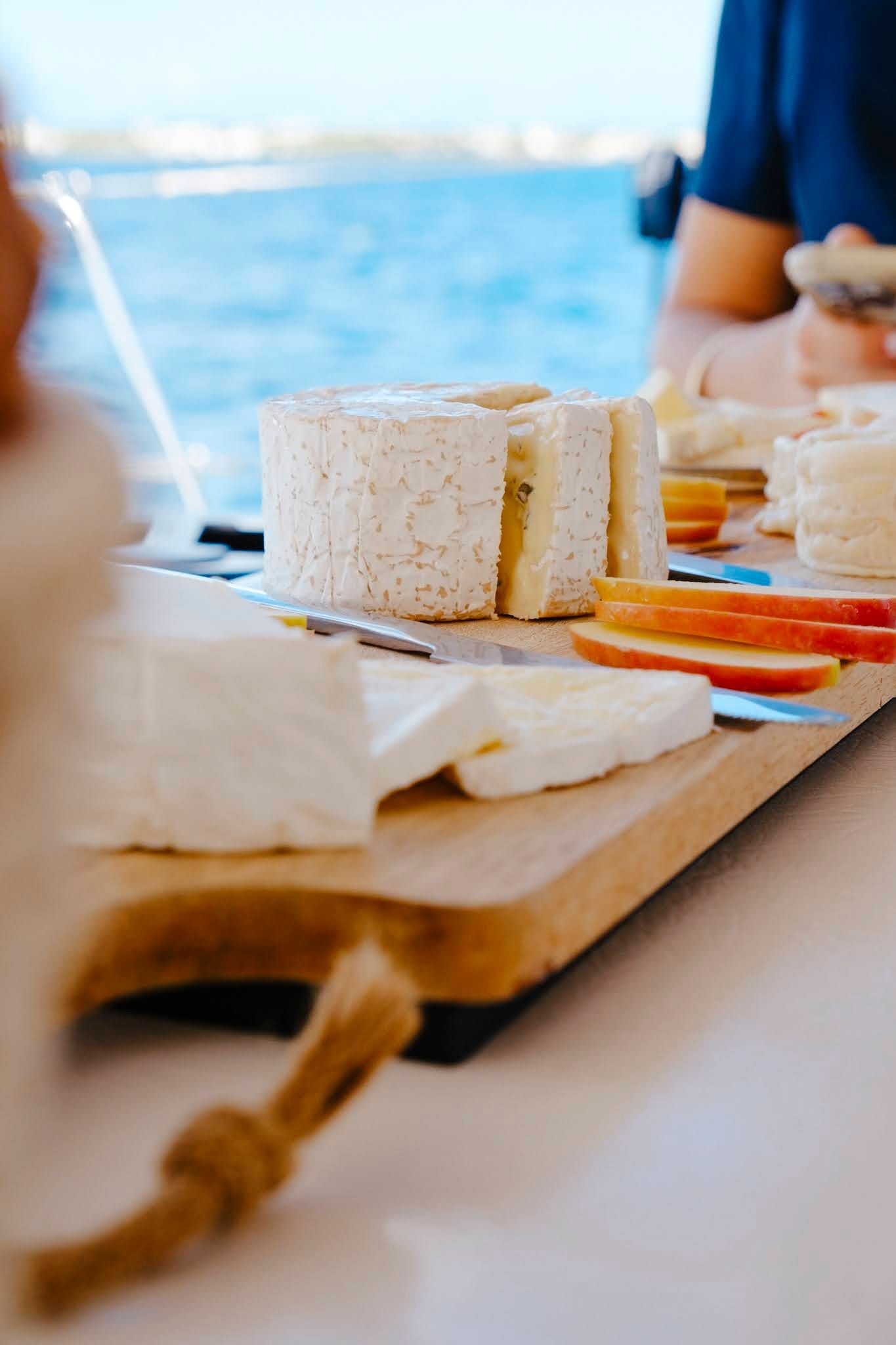 Wooden board with cheese and fruit, against a blue ocean background.