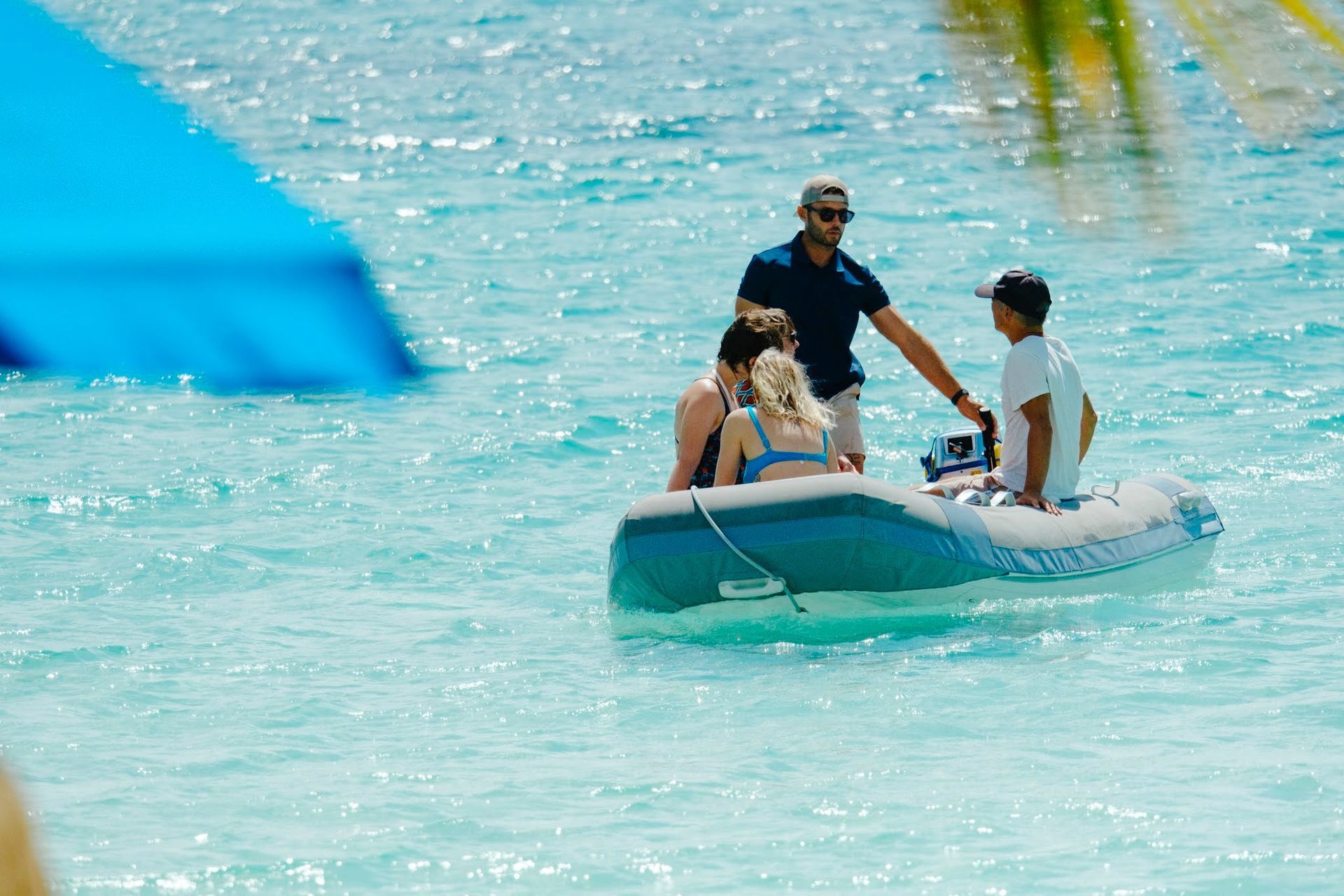 People in an inflatable boat on a turquoise body of water. A man stands at the boat's motor with two seated people.