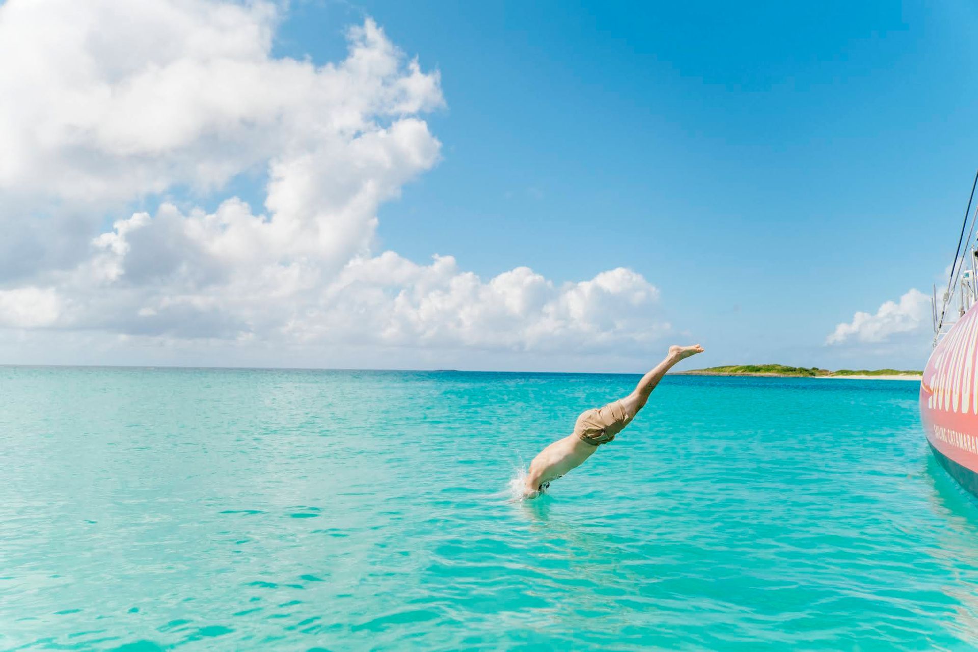 Person diving into clear turquoise water from a boat on a sunny day.