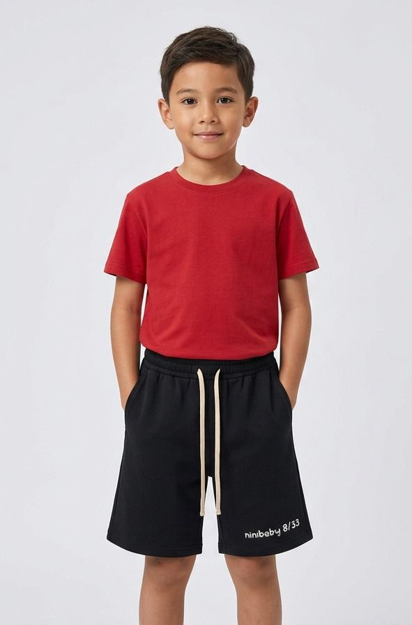 Child in a red T-shirt and black shorts standing against a light gray background.