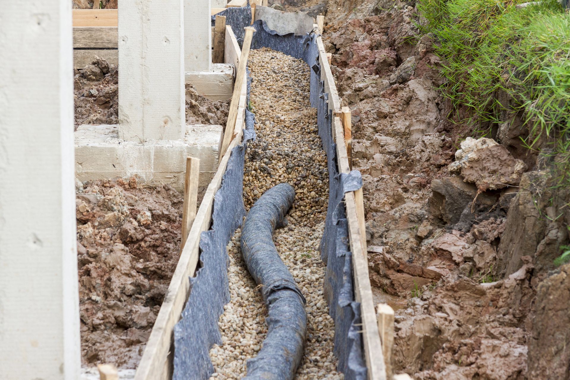Construction trench with drainage pipes and gravel beside a concrete foundation