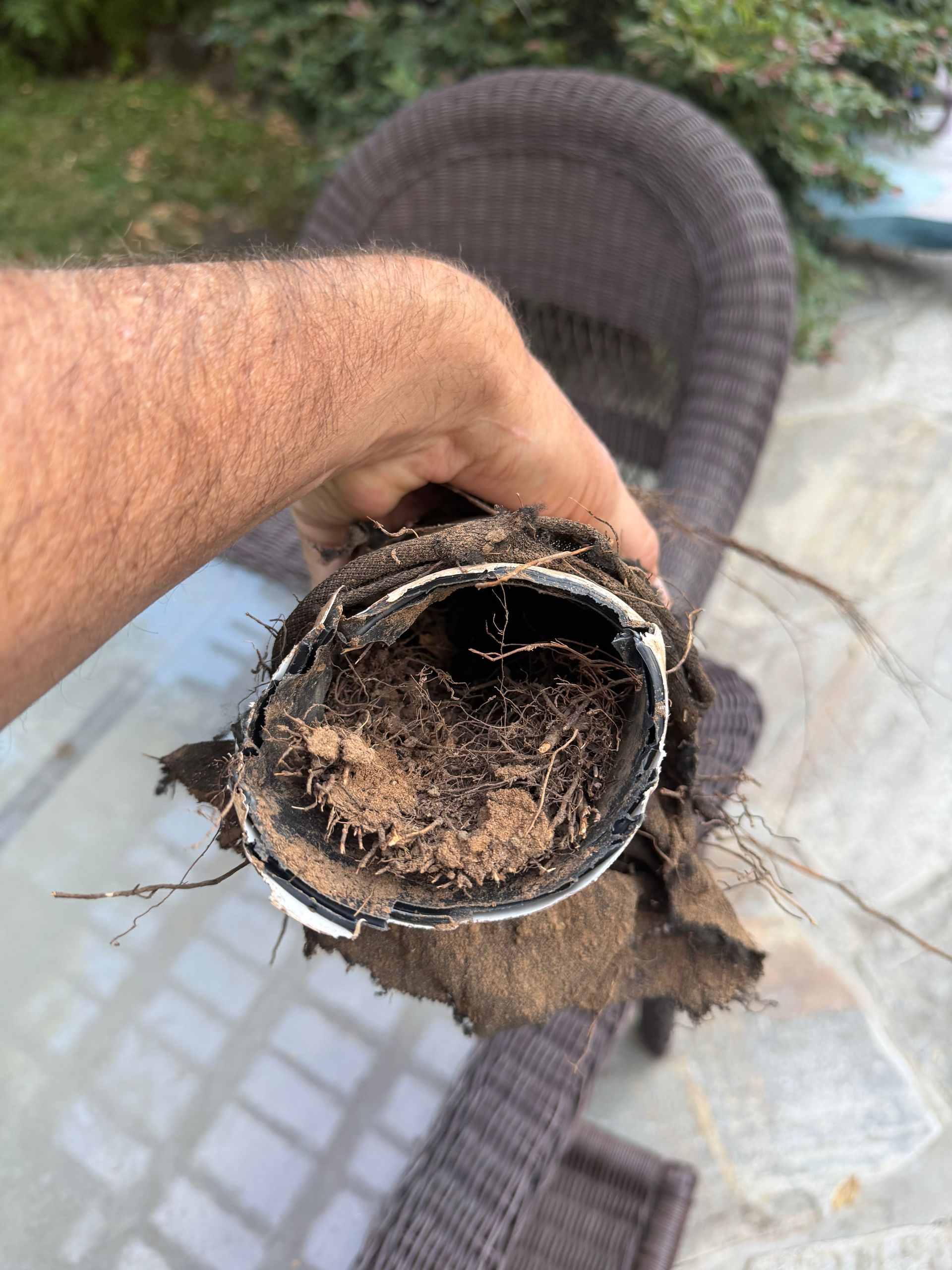 Hand holding a dirty, damaged hose or pipe with debris inside on a patio outdoors