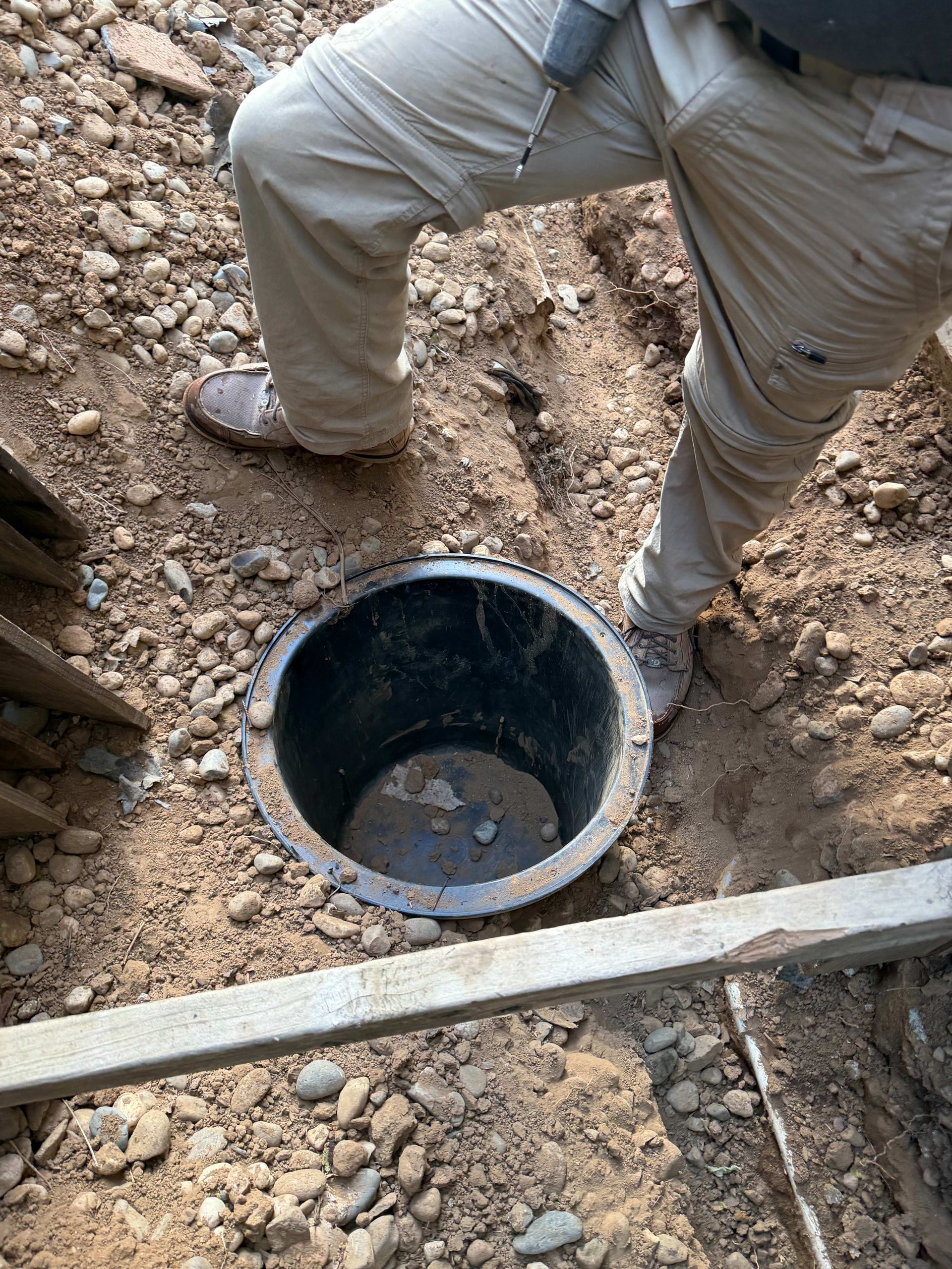 Worker standing in a dirt trench beside a black utility pipe opening