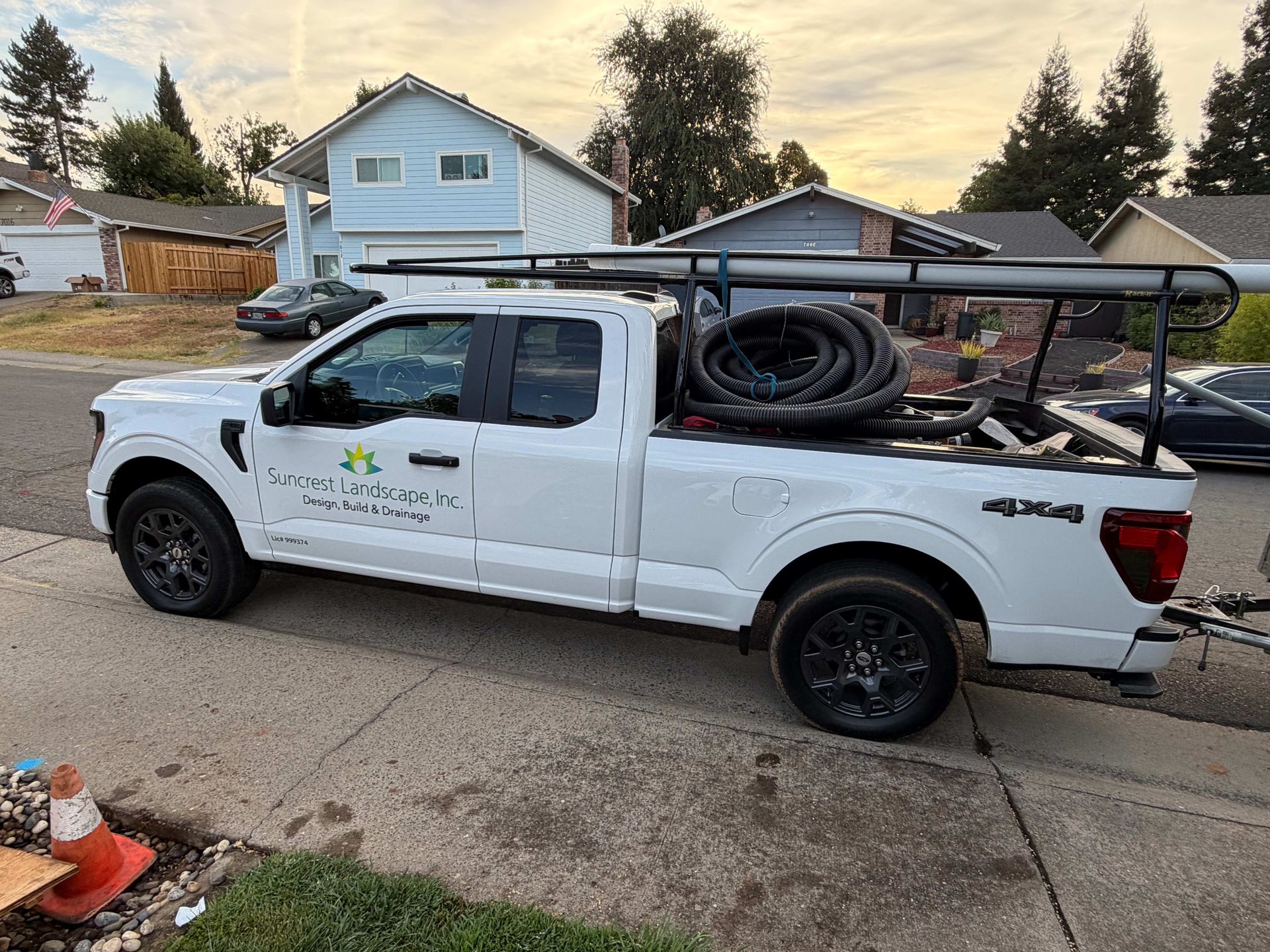 White pickup truck with company logo and ladder rack, parked in a residential driveway at dusk