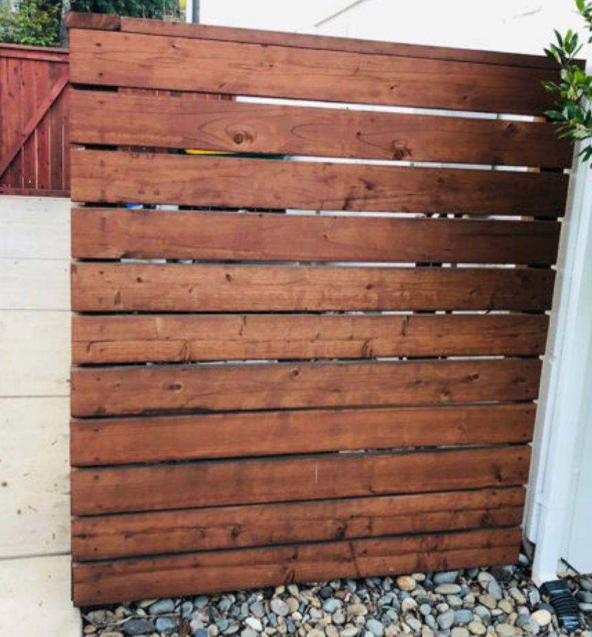 Wooden slat privacy fence with reddish-brown boards above a gray pebble ground