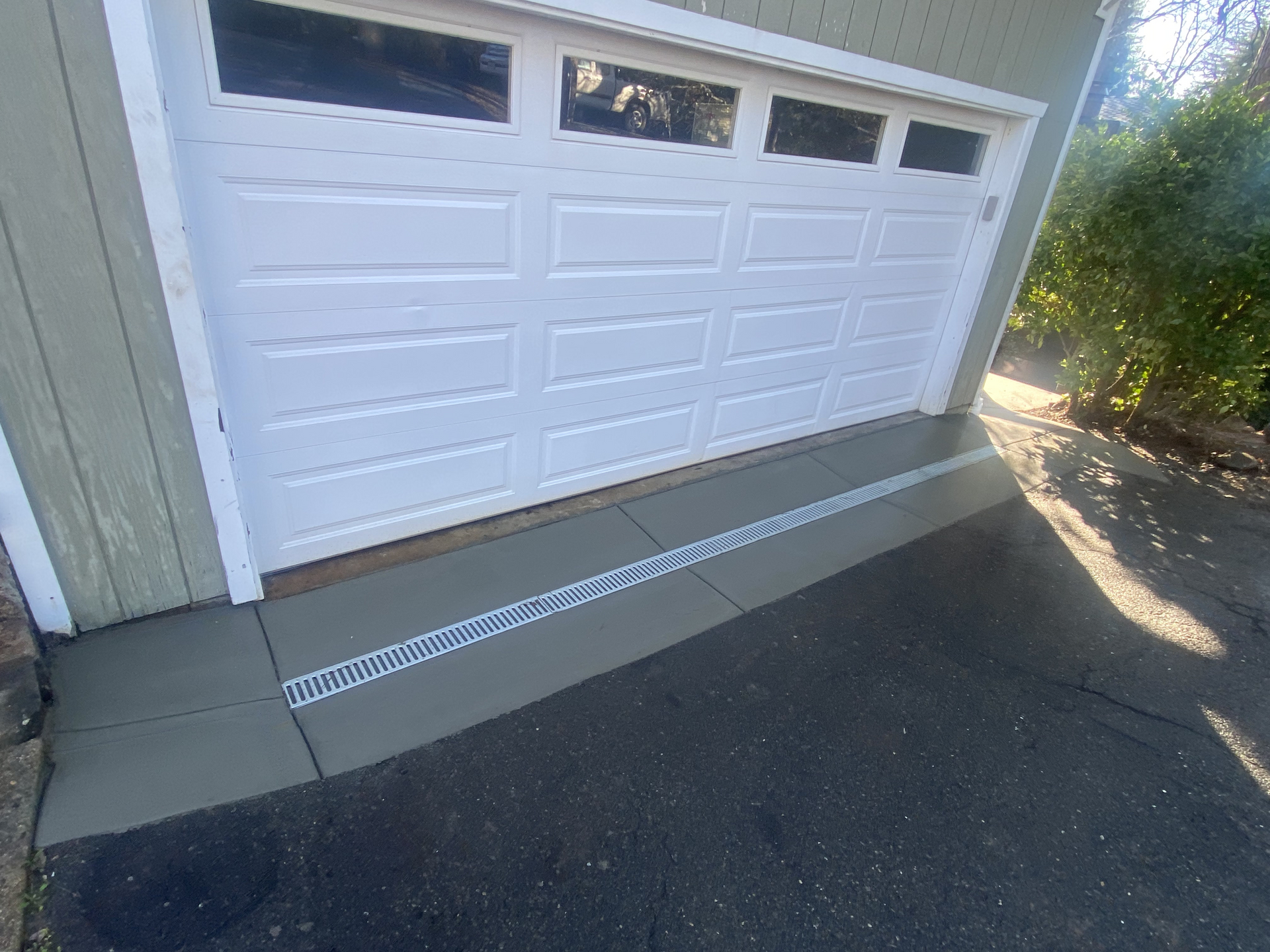 White two-car garage with a sloped driveway and drainage grate at the base of the door.