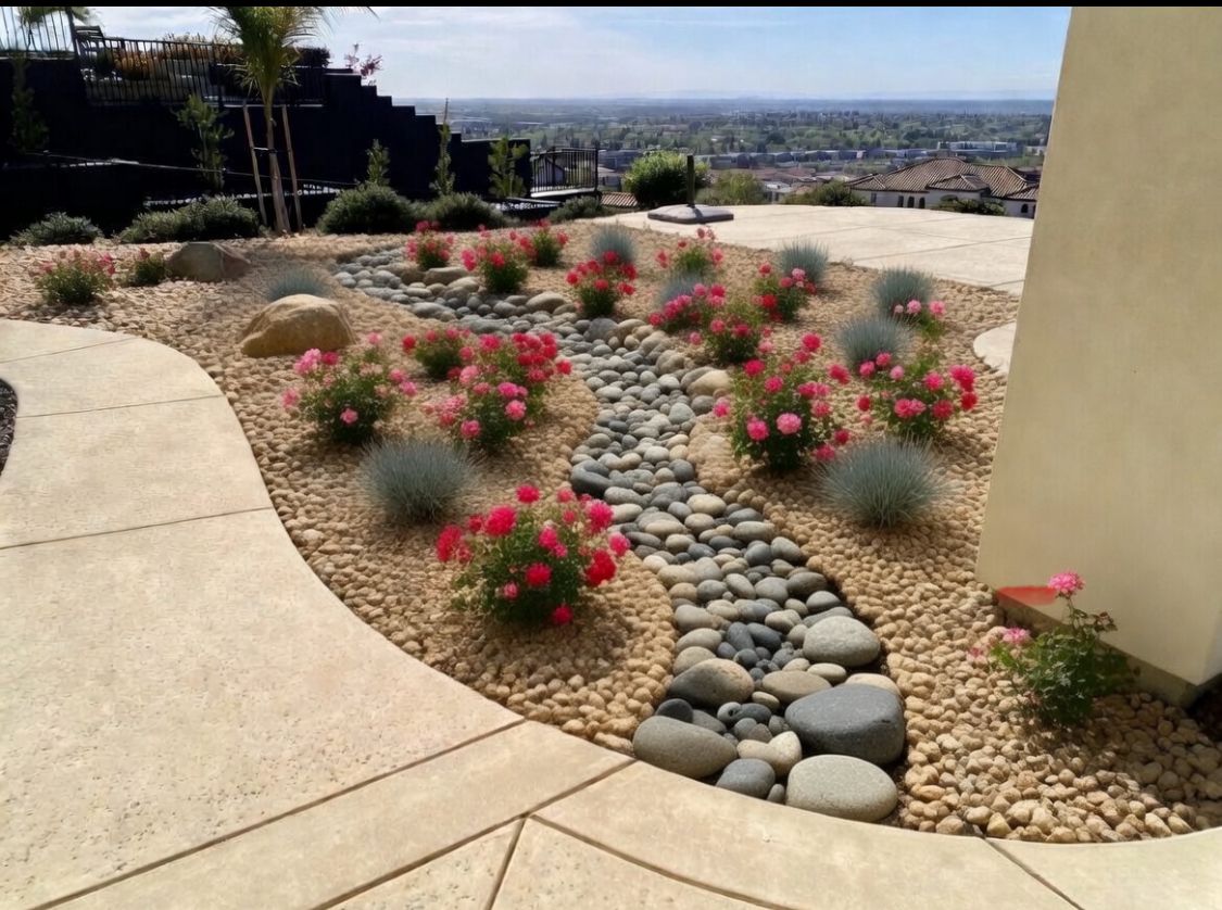Desert garden with pink flowering shrubs, stone path, and city view beyond a patio