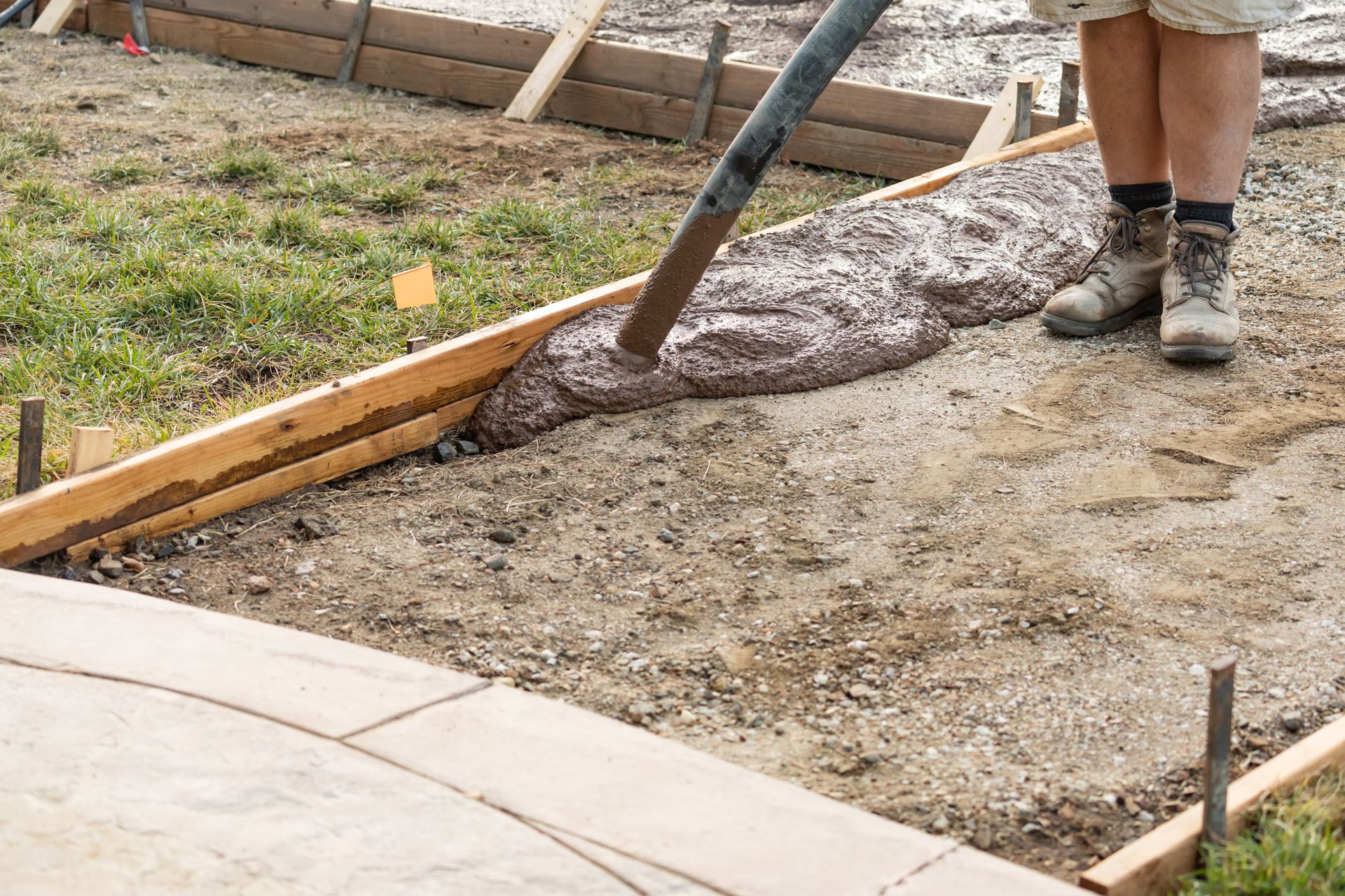Worker pouring wet concrete into a wooden form at a construction site
