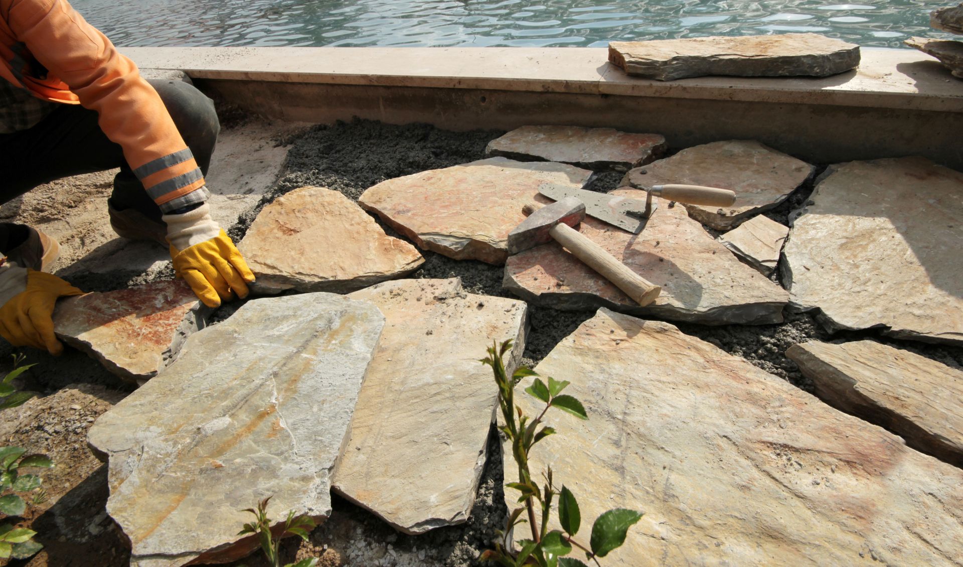 Worker in yellow gloves laying flat stones beside a water feature