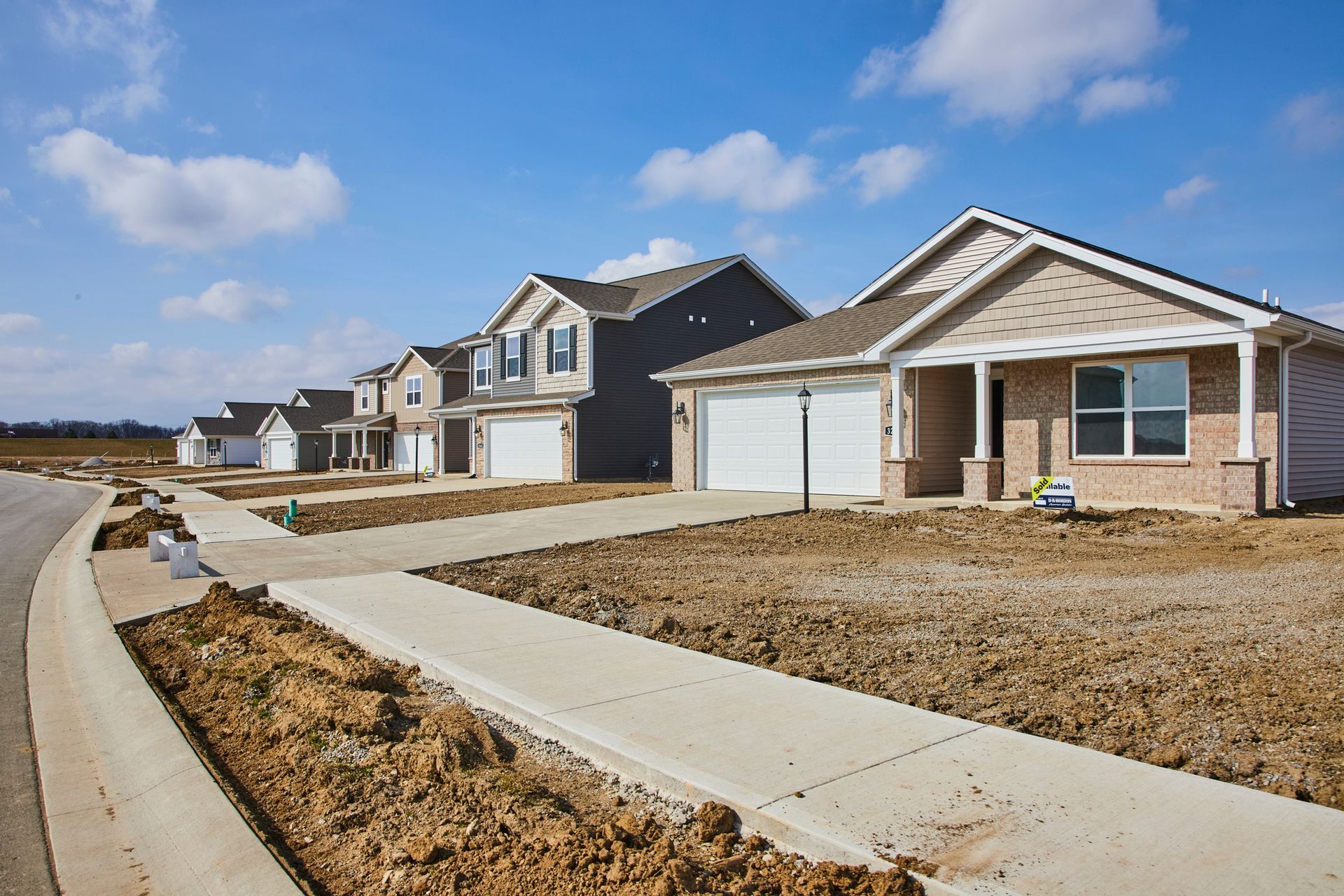 Row of newly built suburban houses with concrete sidewalks and bare front yards under a blue sky
