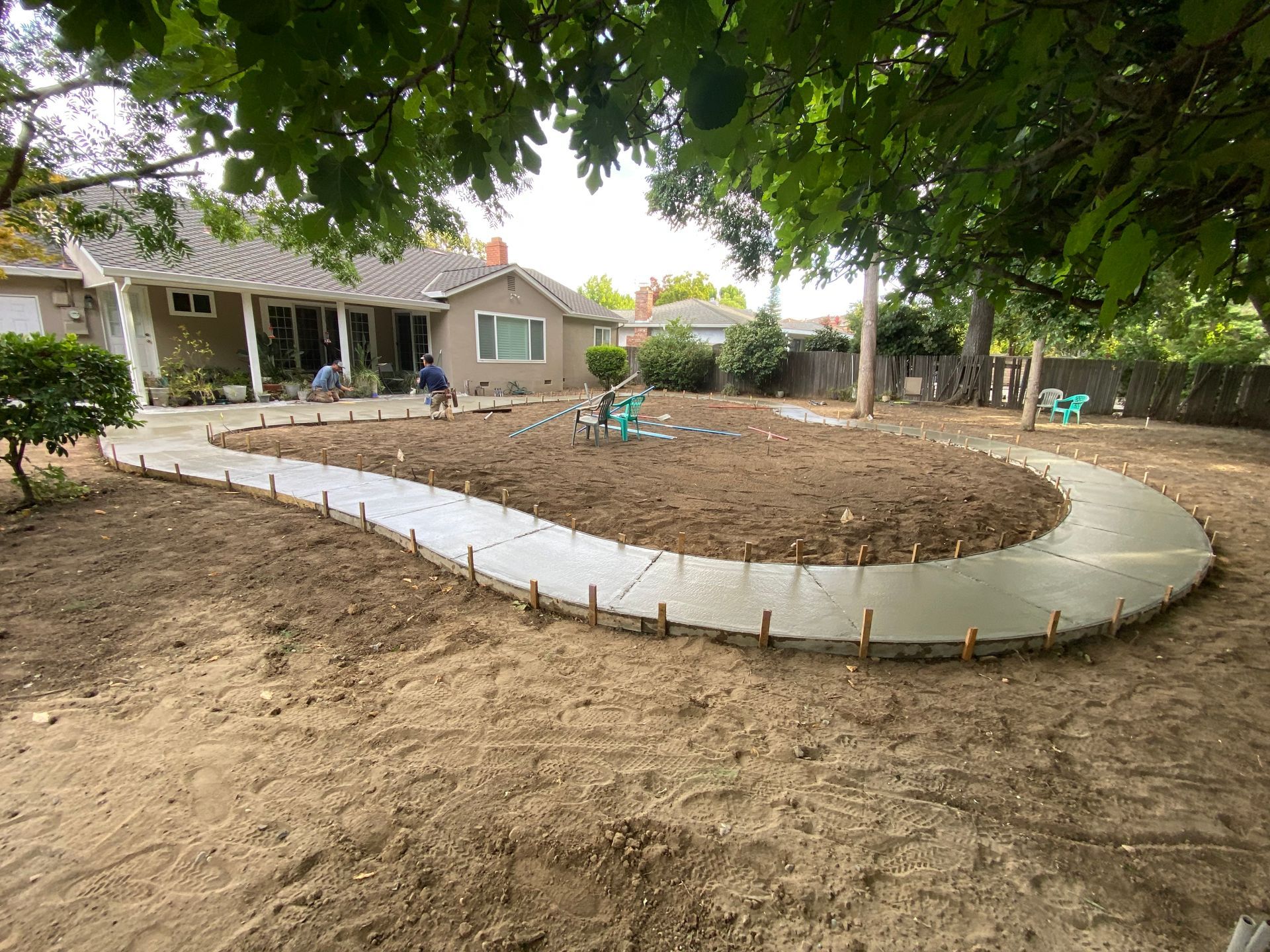 Curved concrete path around a dirt yard with a house and shaded trees in the background