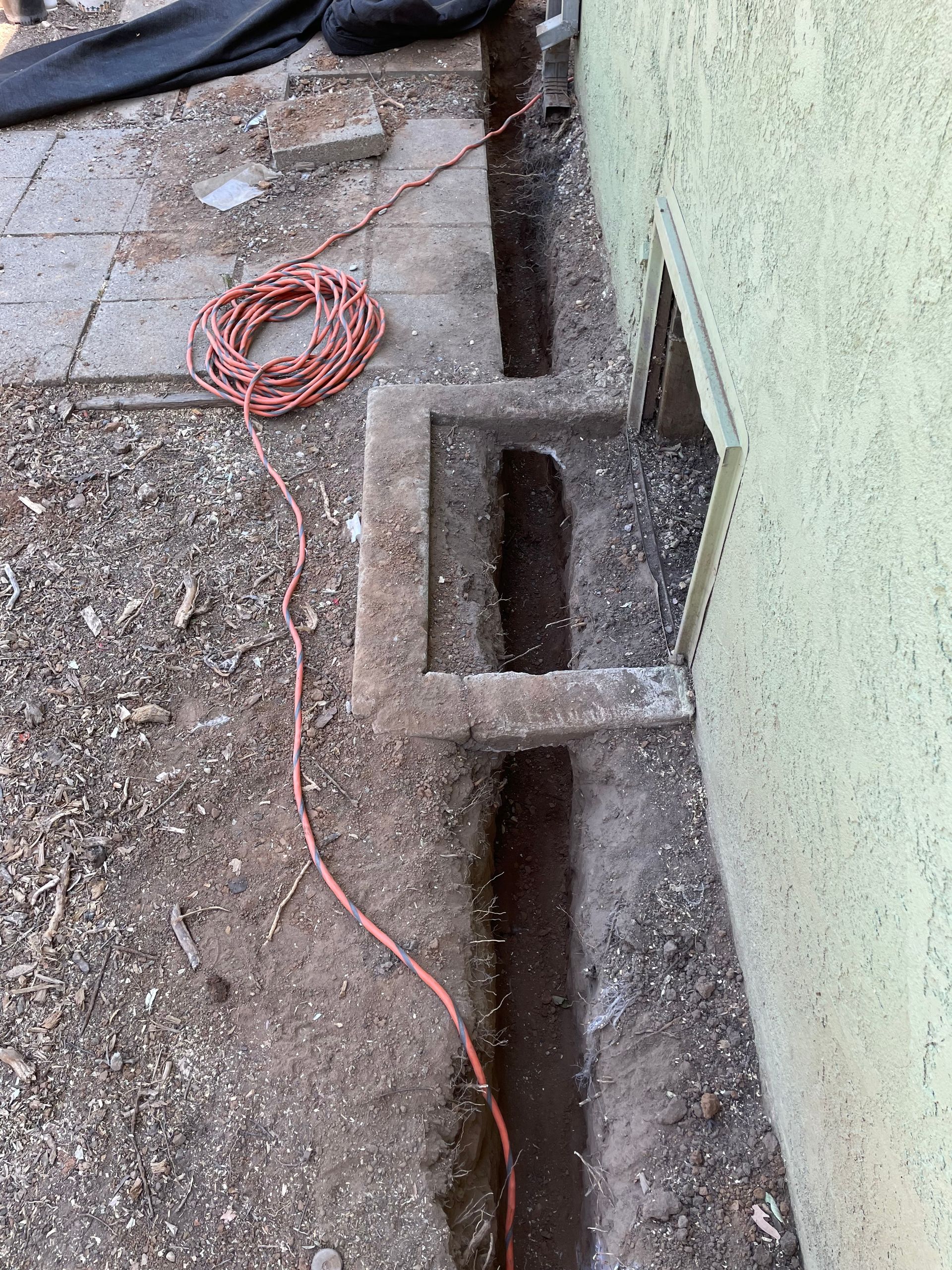 Coiled orange cable on a gravel path beside a green wall and concrete drainage channel