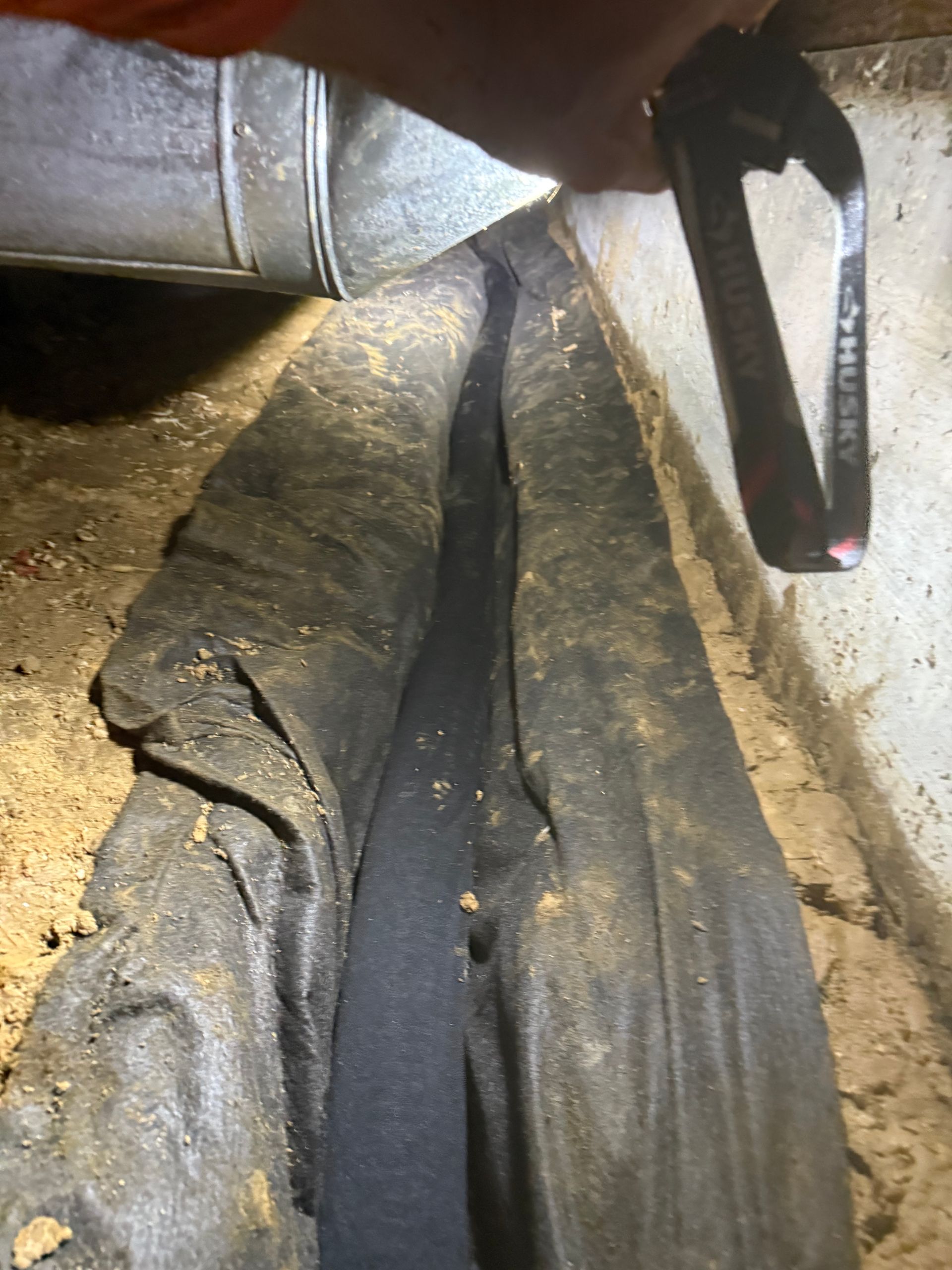 Dirty black fabric/tarp stuffed under a vehicle near a wheel well, with a tool handle at top right
