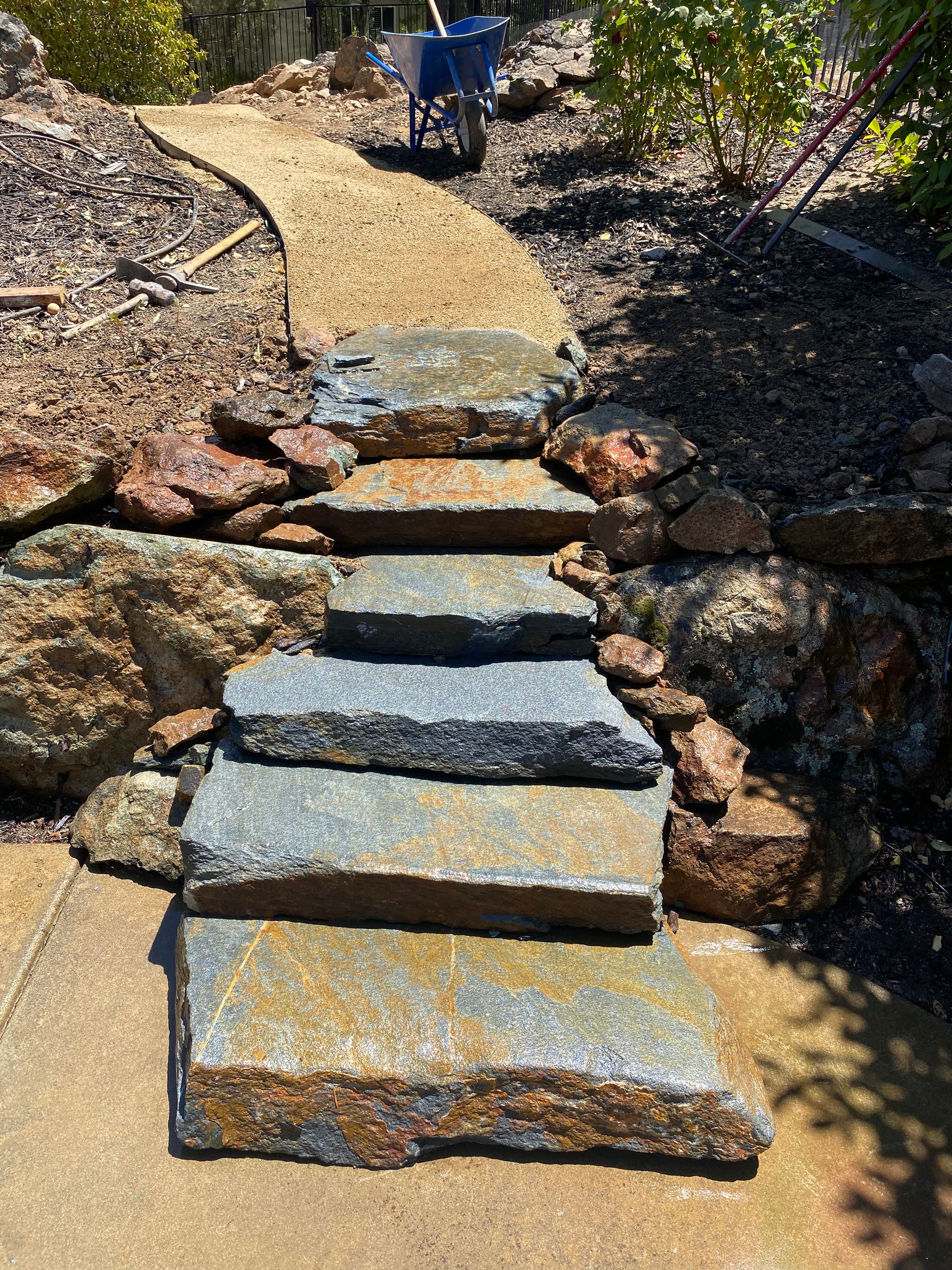 Stone steps on a garden path, bordered by rocks and mulch, leading uphill