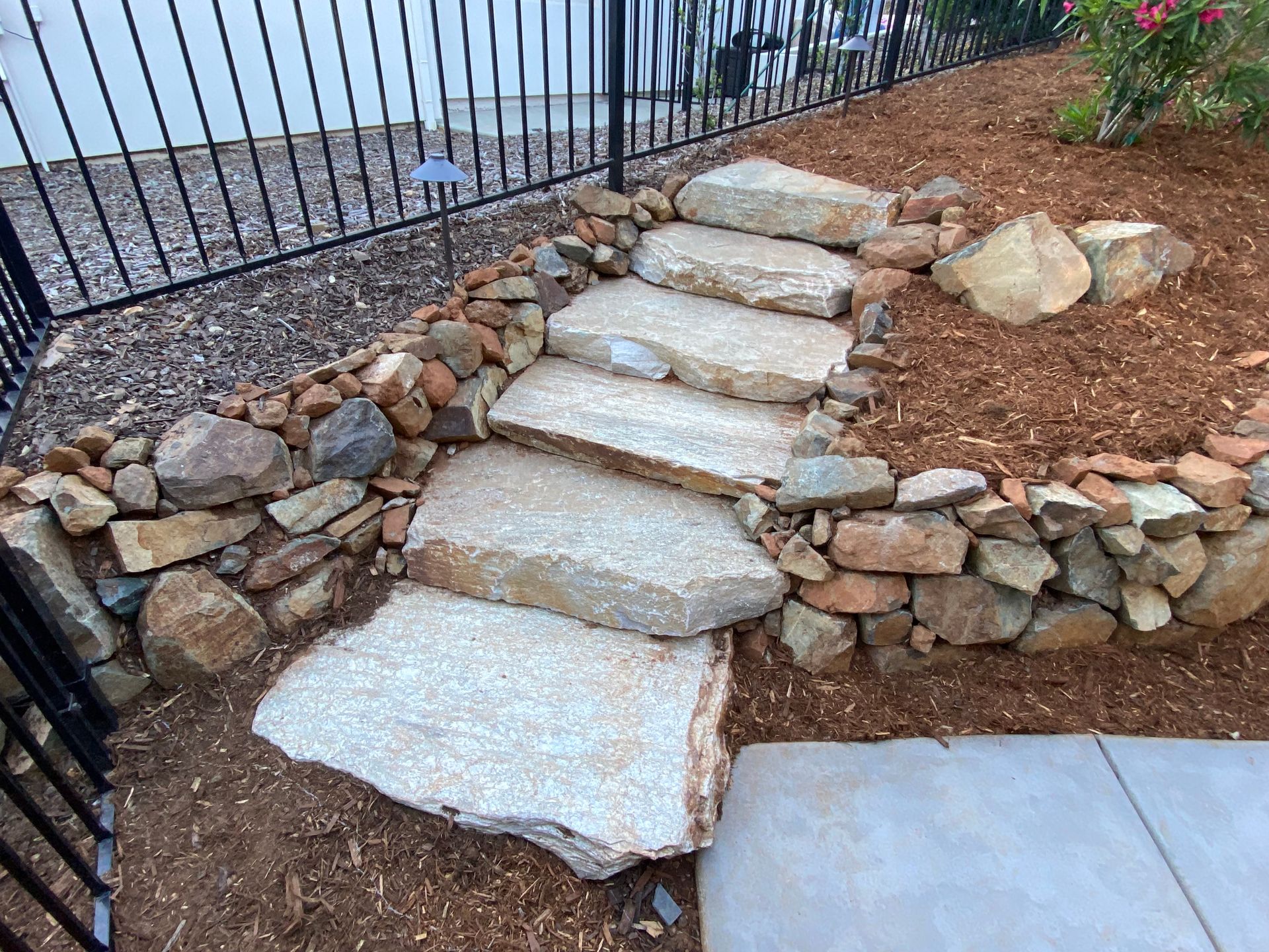 Stone steps in a landscaped garden beside a metal fence and patio walkway