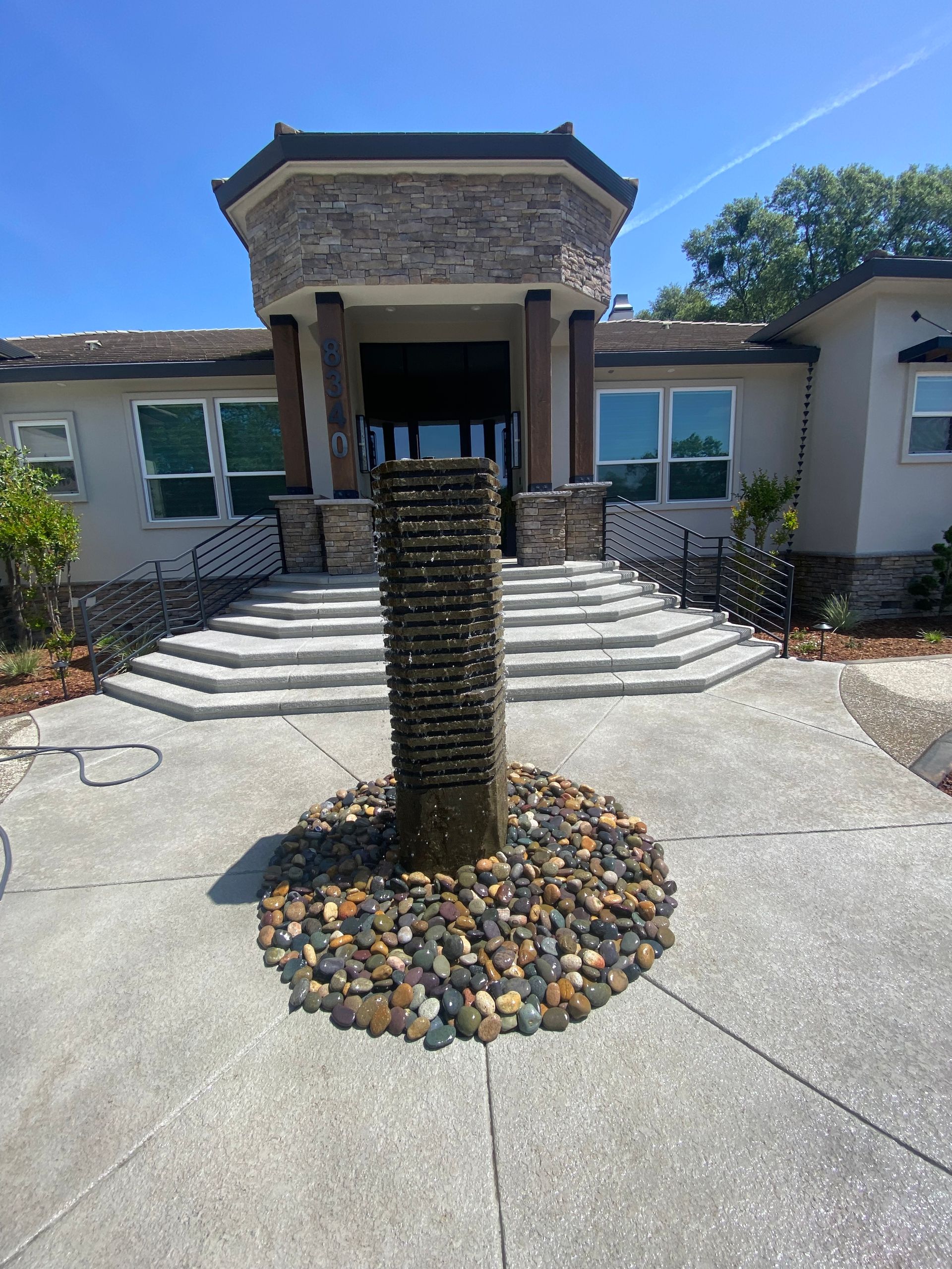 Front view of a house with stone steps and a tall decorative pole in the driveway circle with rocks.