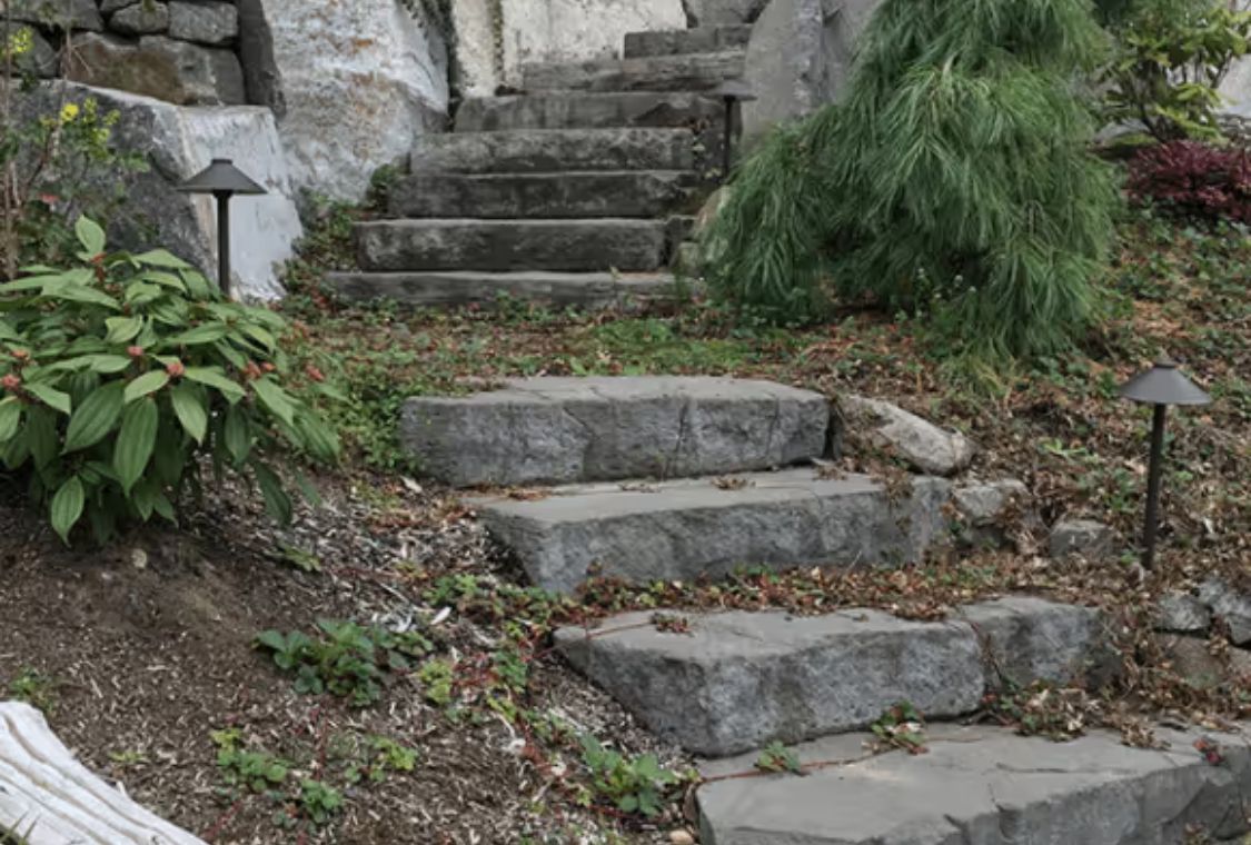Stone garden steps beside greenery and a stone wall