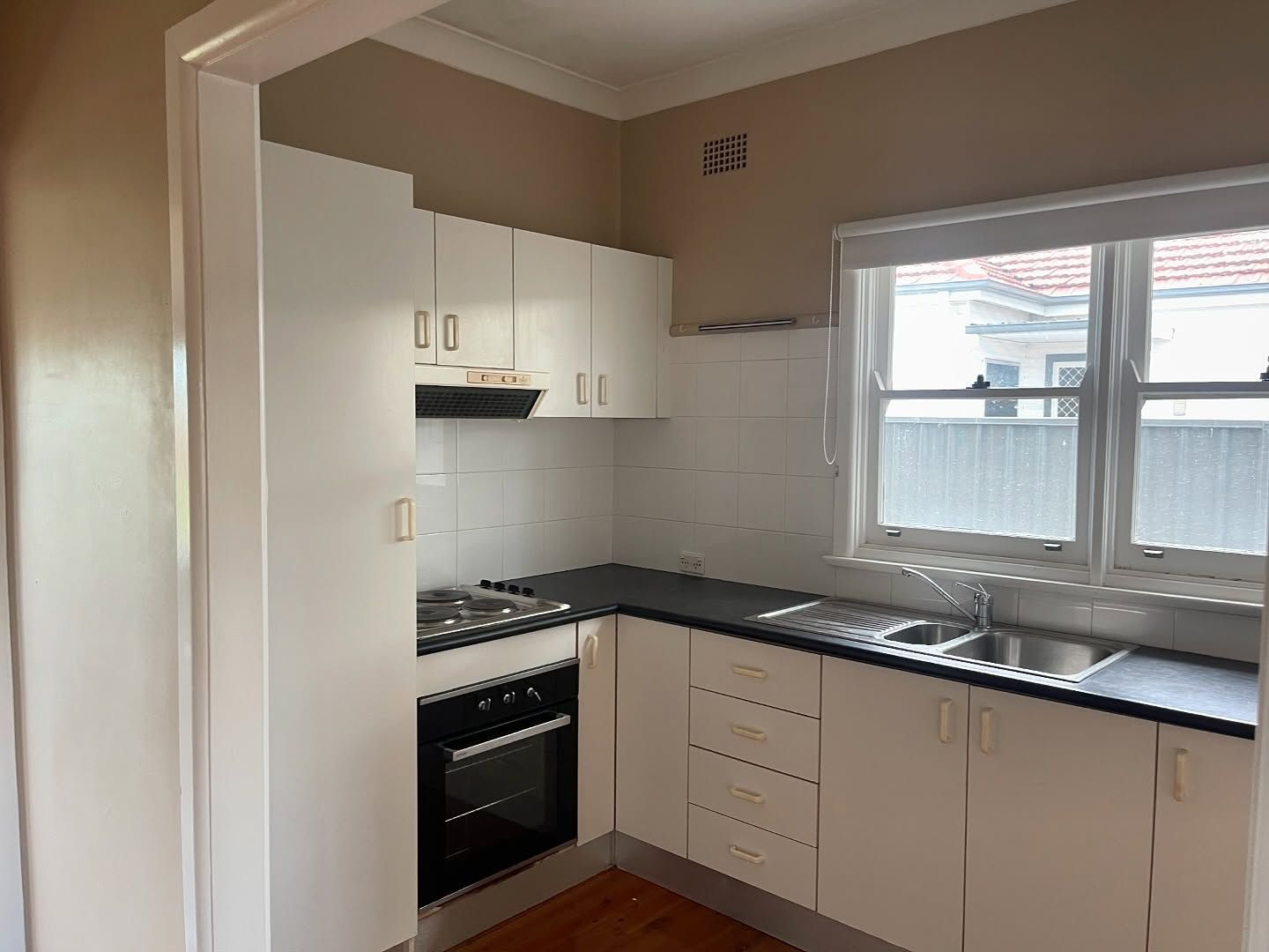 Small White Kitchen With Black Countertops, a Window, and Wood Flooring — Ecowave Solutions Asbestos Removal In Gosford, NSW
