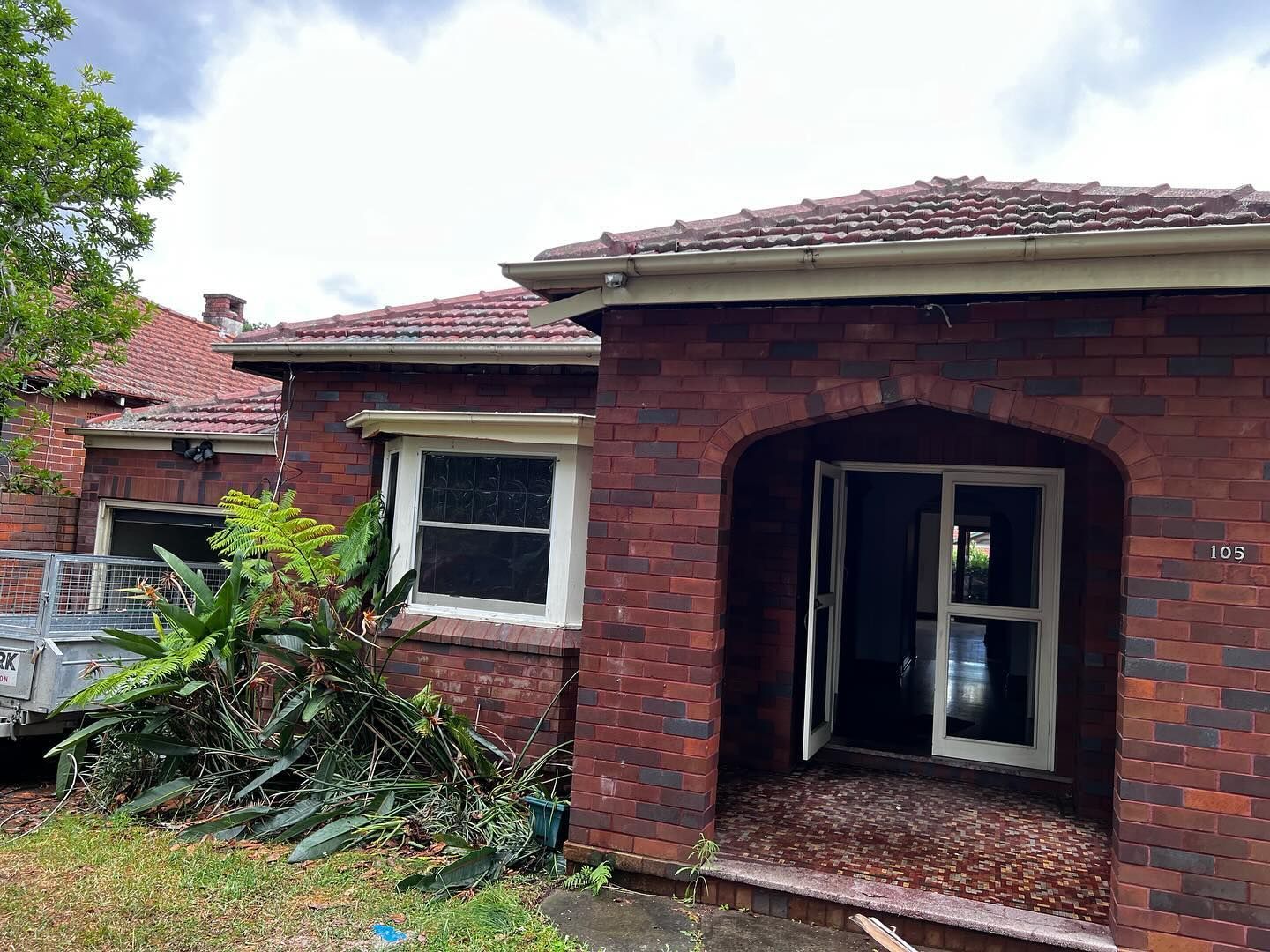 Red Brick House With an Open Doorway and Window, Overgrown Foliage — Ecowave Solutions Asbestos Removal n Gosford, NSW