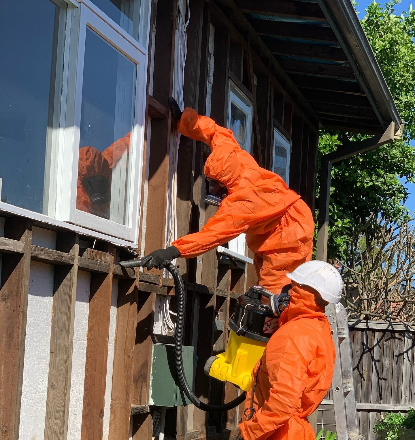 Two People in Orange Protective Suits Working on a House Exterior — Ecowave Solutions Asbestos Removal In Gosford, NSW