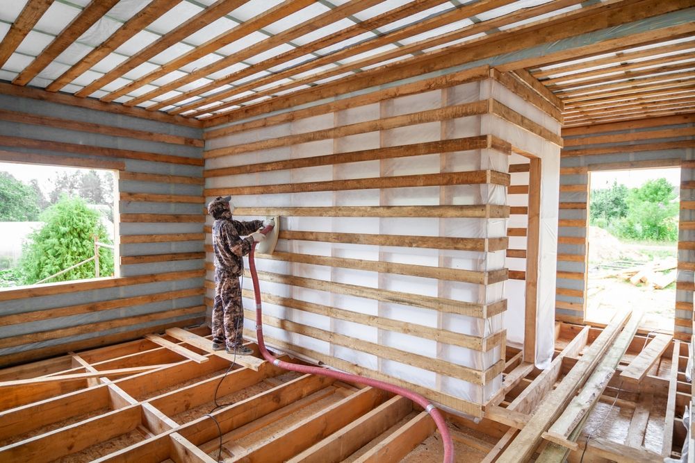 Interior of a house under construction with exposed wooden framing and a worker installing insulation panels