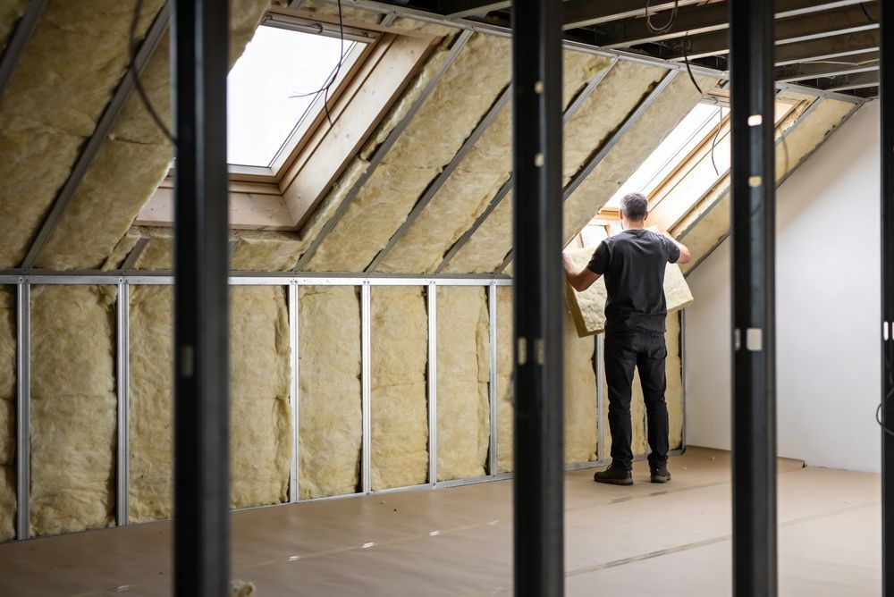 Worker installing insulation in an unfinished attic framed with exposed studs and skylights
