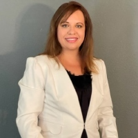 A woman in a white jacket and black top is smiling for the camera.