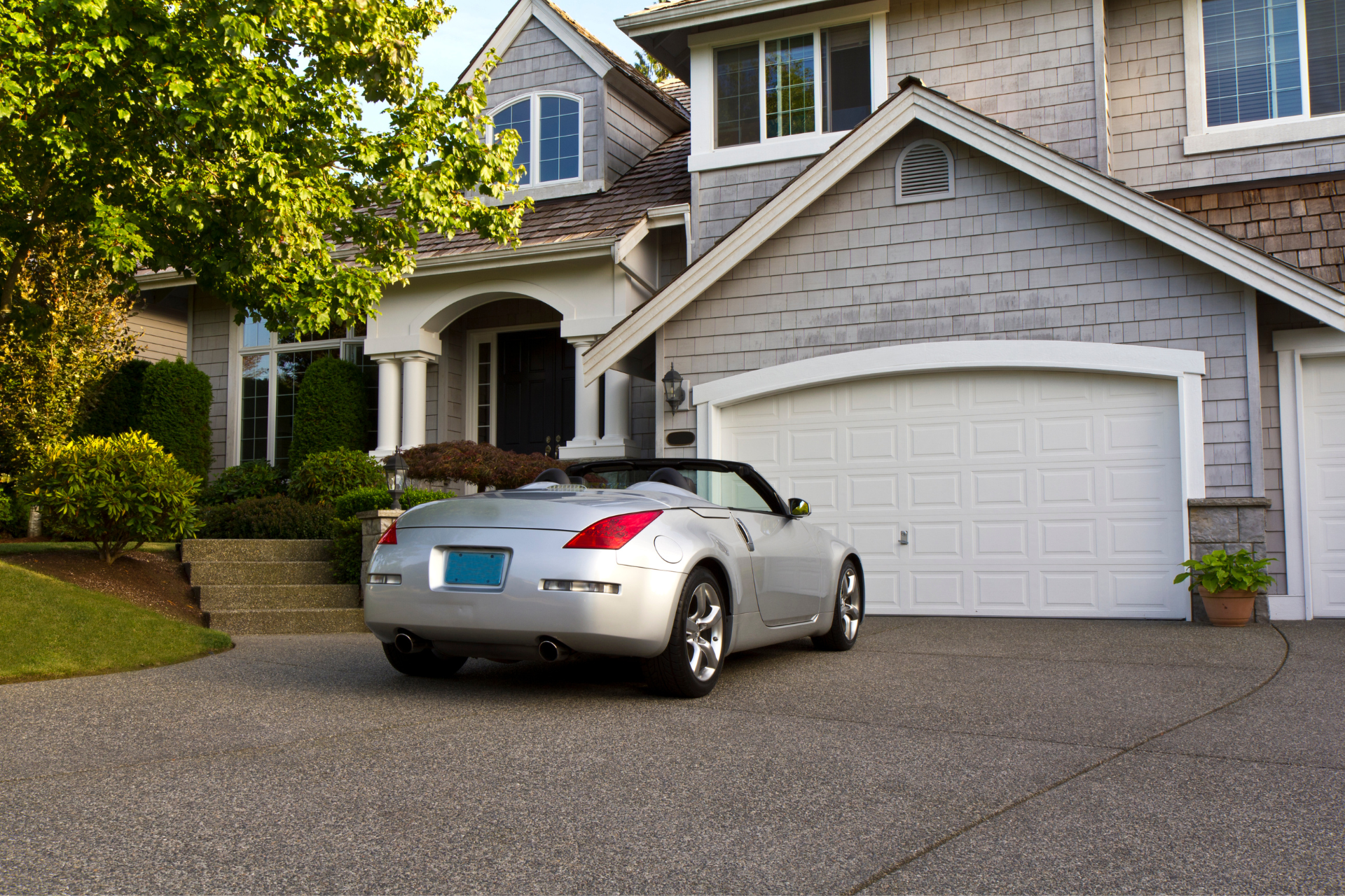 A silver convertible car is parked in front of a large house.