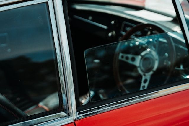 A close up of a red car with a steering wheel in the window.