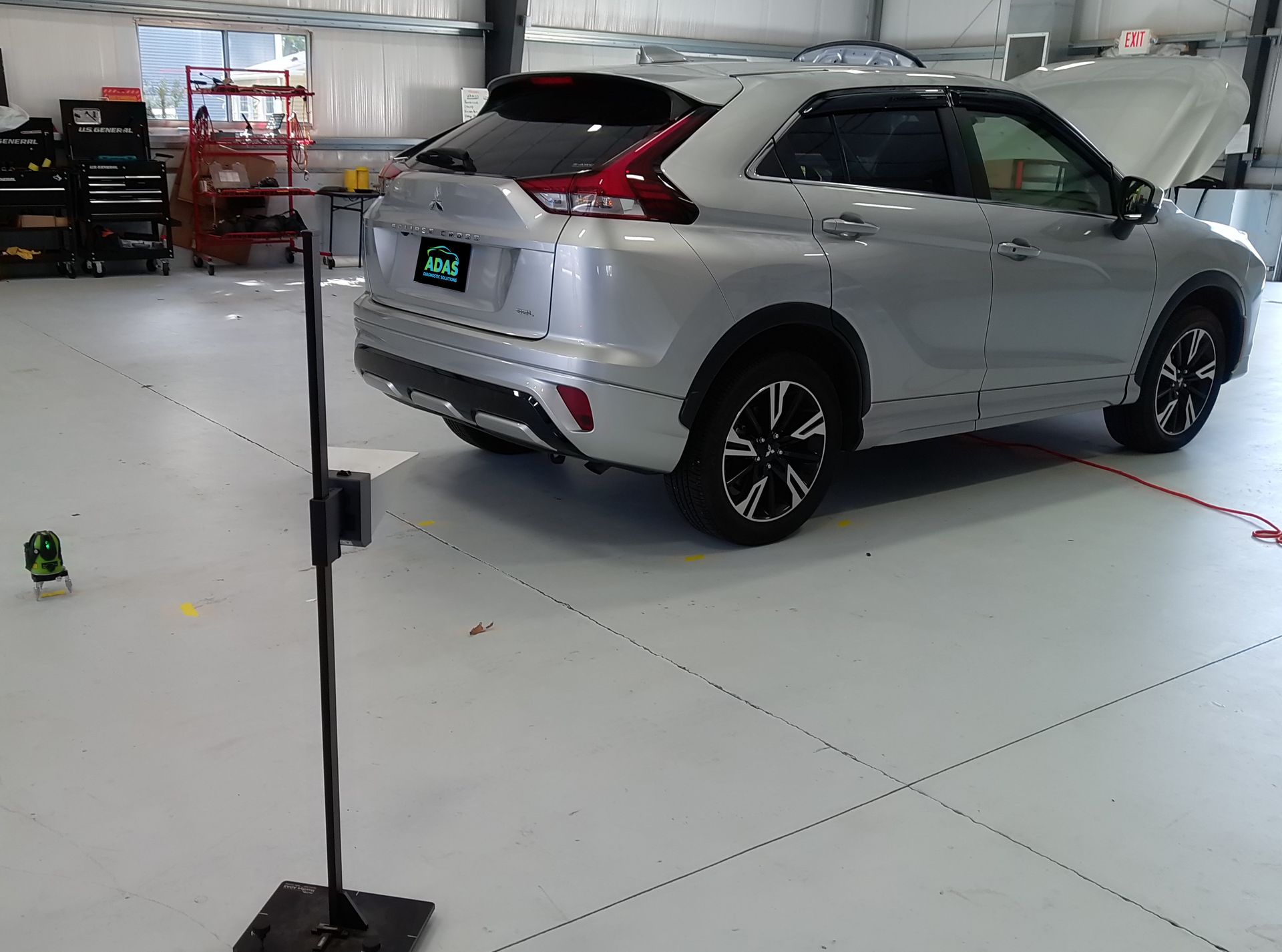 A silver car is parked in a garage with the hood up.