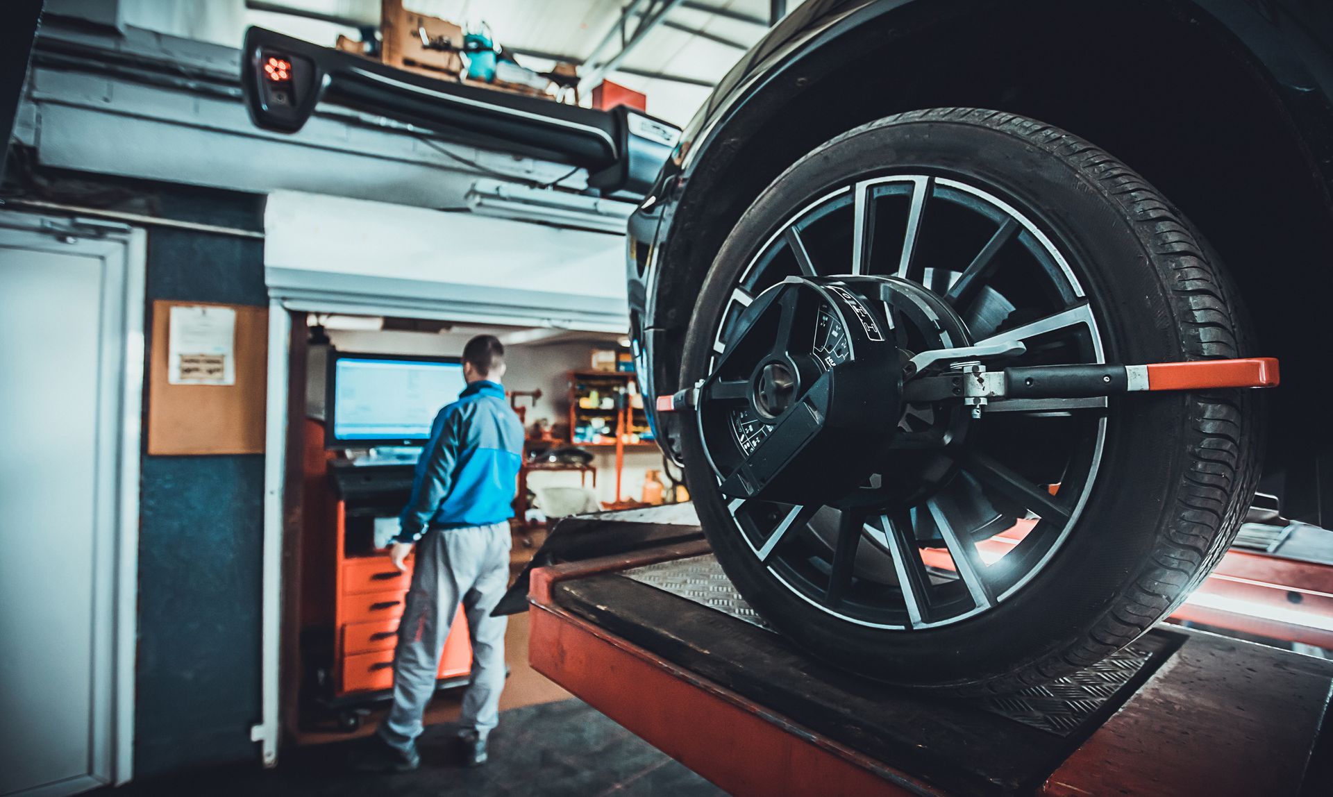 A man is standing next to a car on a lift in a garage.